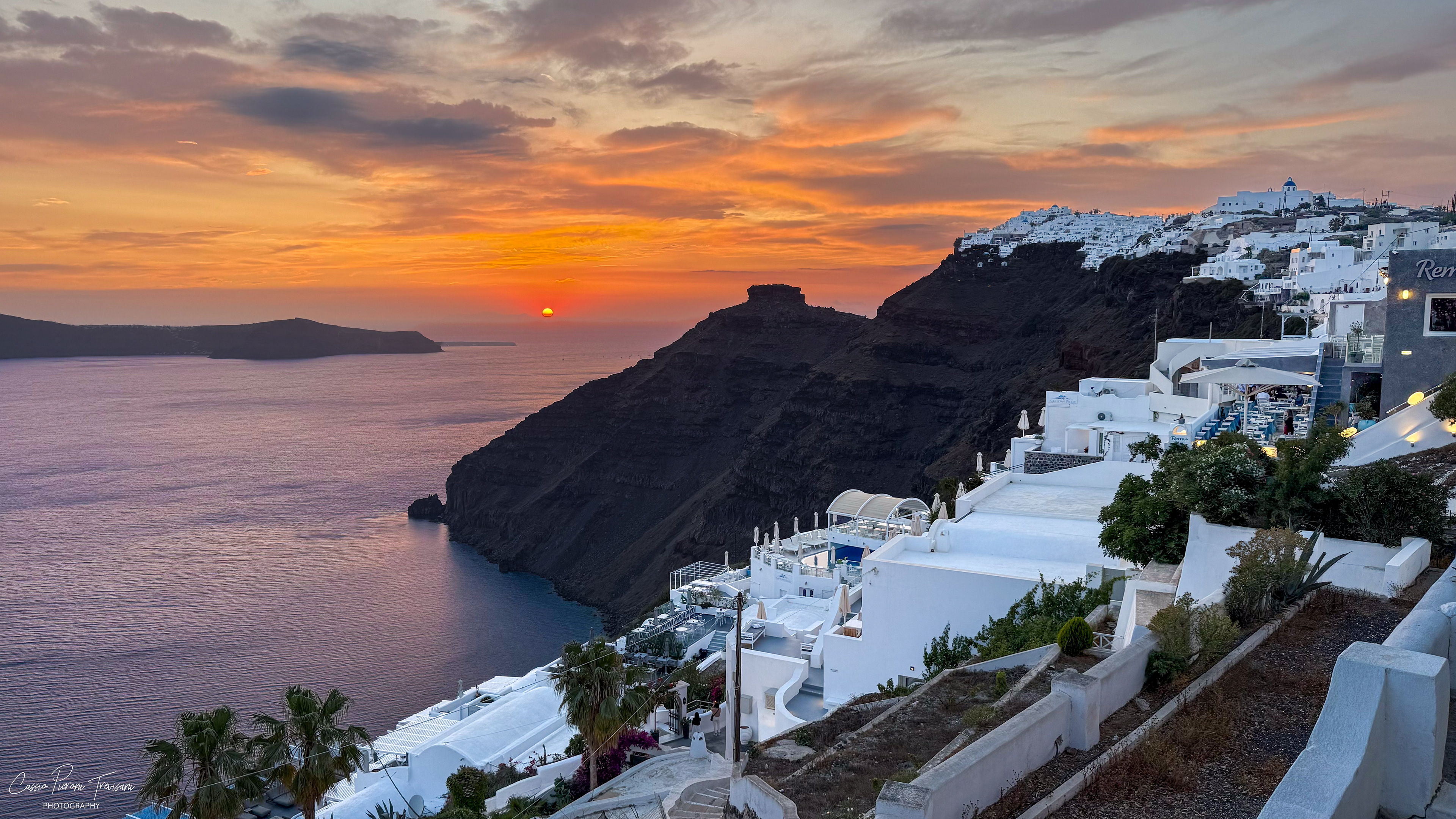 Sunset over Santorini paints the sky in warm tones as the cliffs and Imerovigli fade into silhouette.