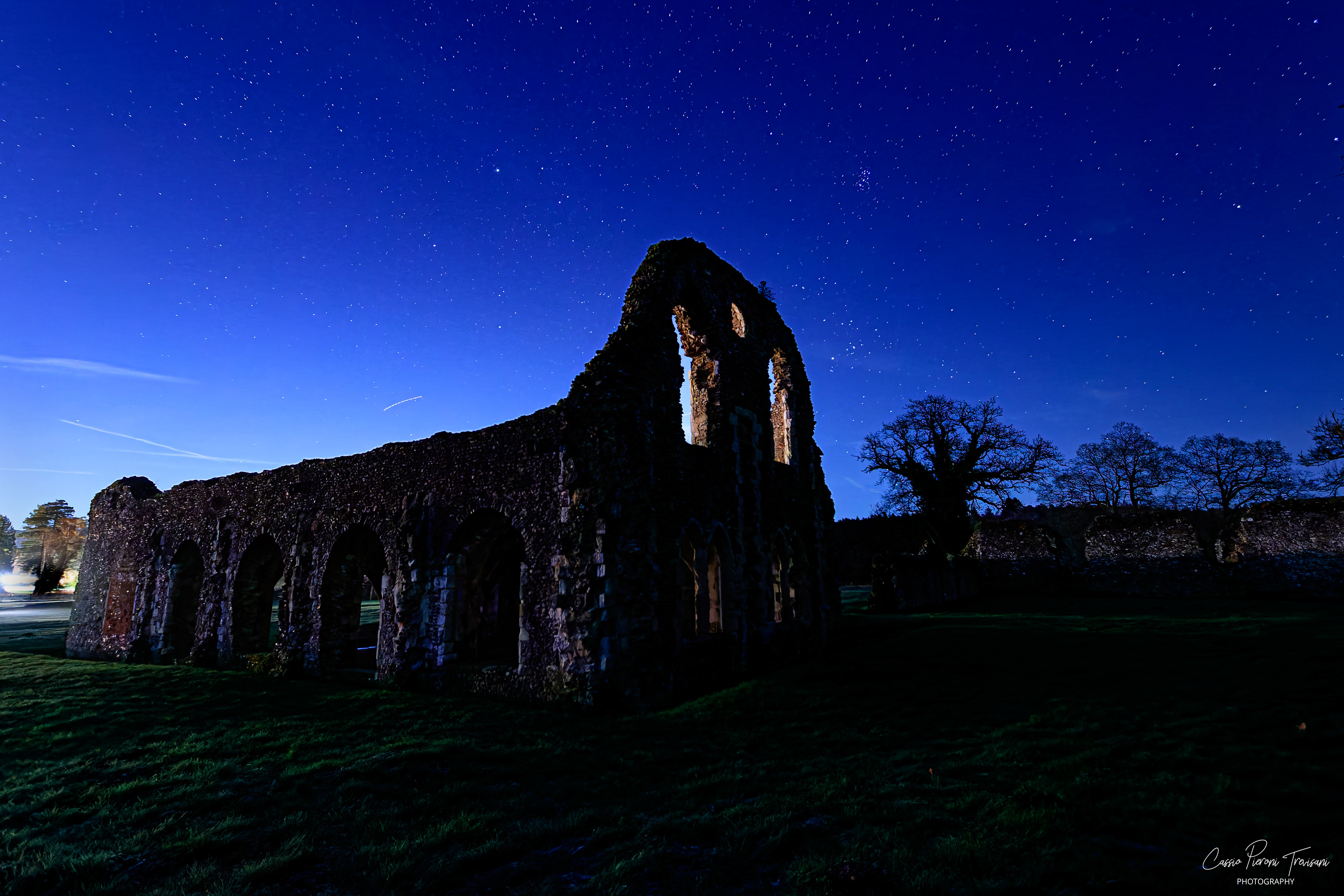Wide night view of Waverley Abbey ruins lit from behind beneath a star-filled sky.