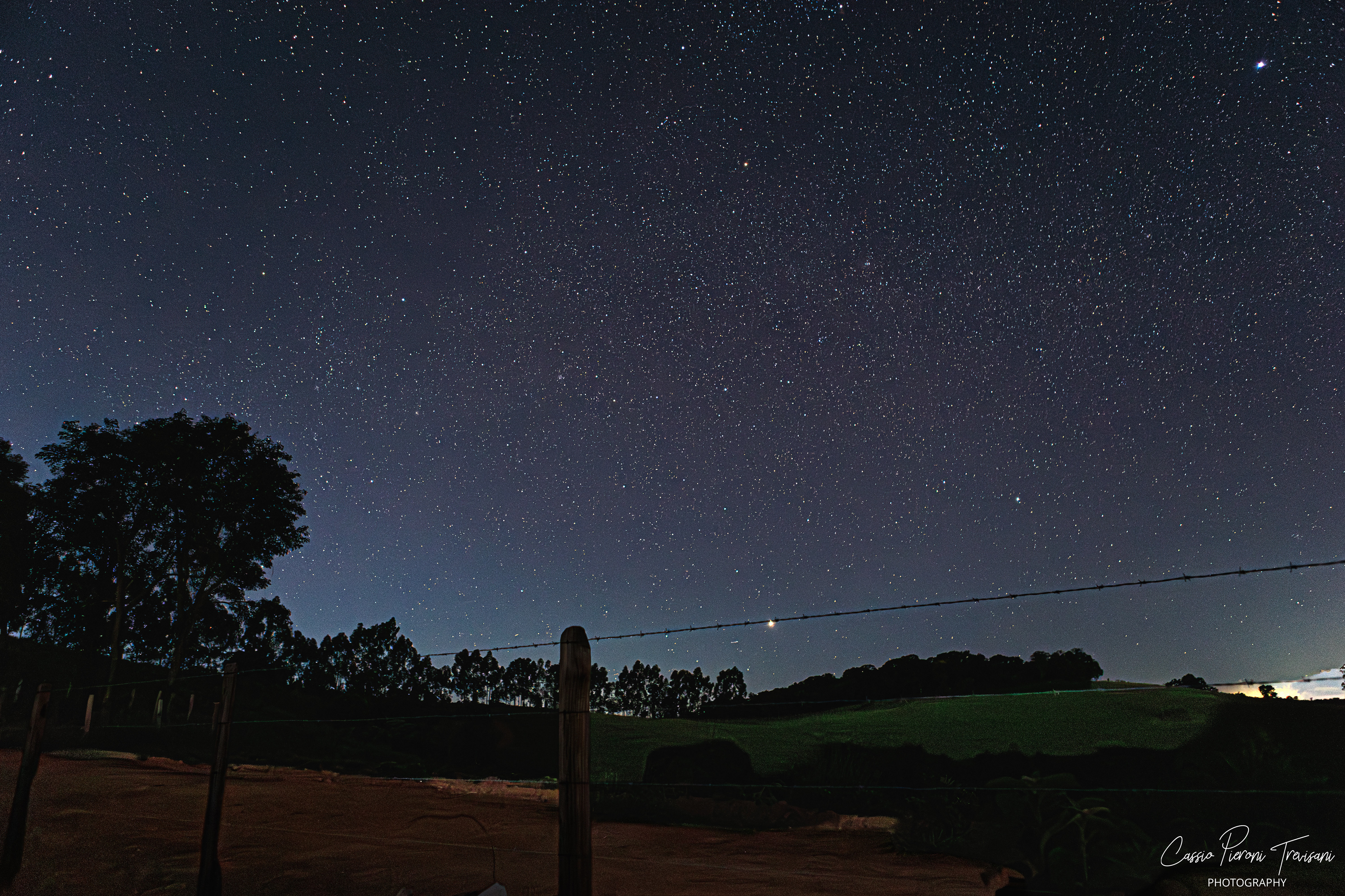 Starry sky over Mirante de Albertina with illuminated foreground and distant landscape.
