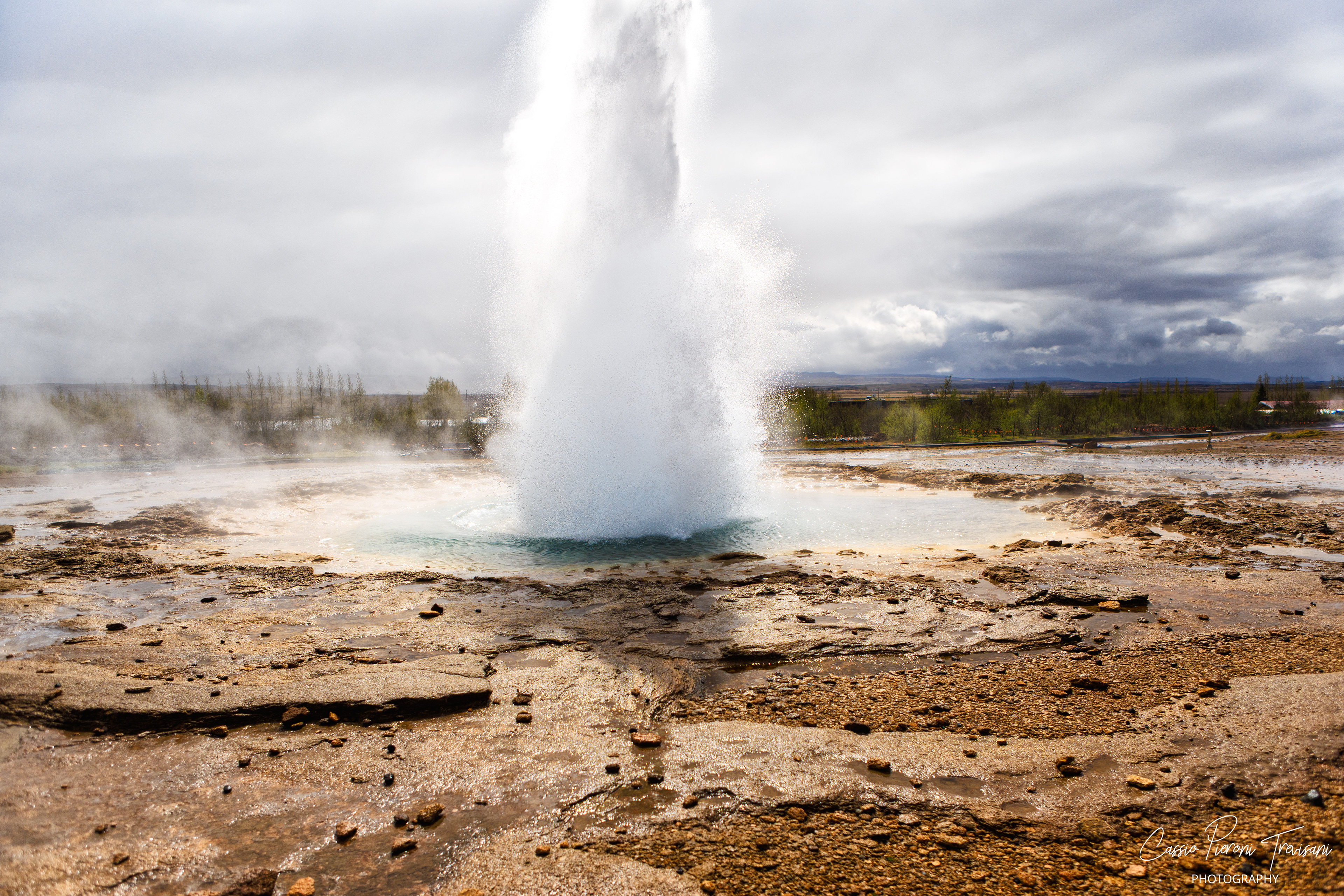 Strokkur erupts from the geothermal field, launching boiling water into the air as steam rises across the volcanic plain.