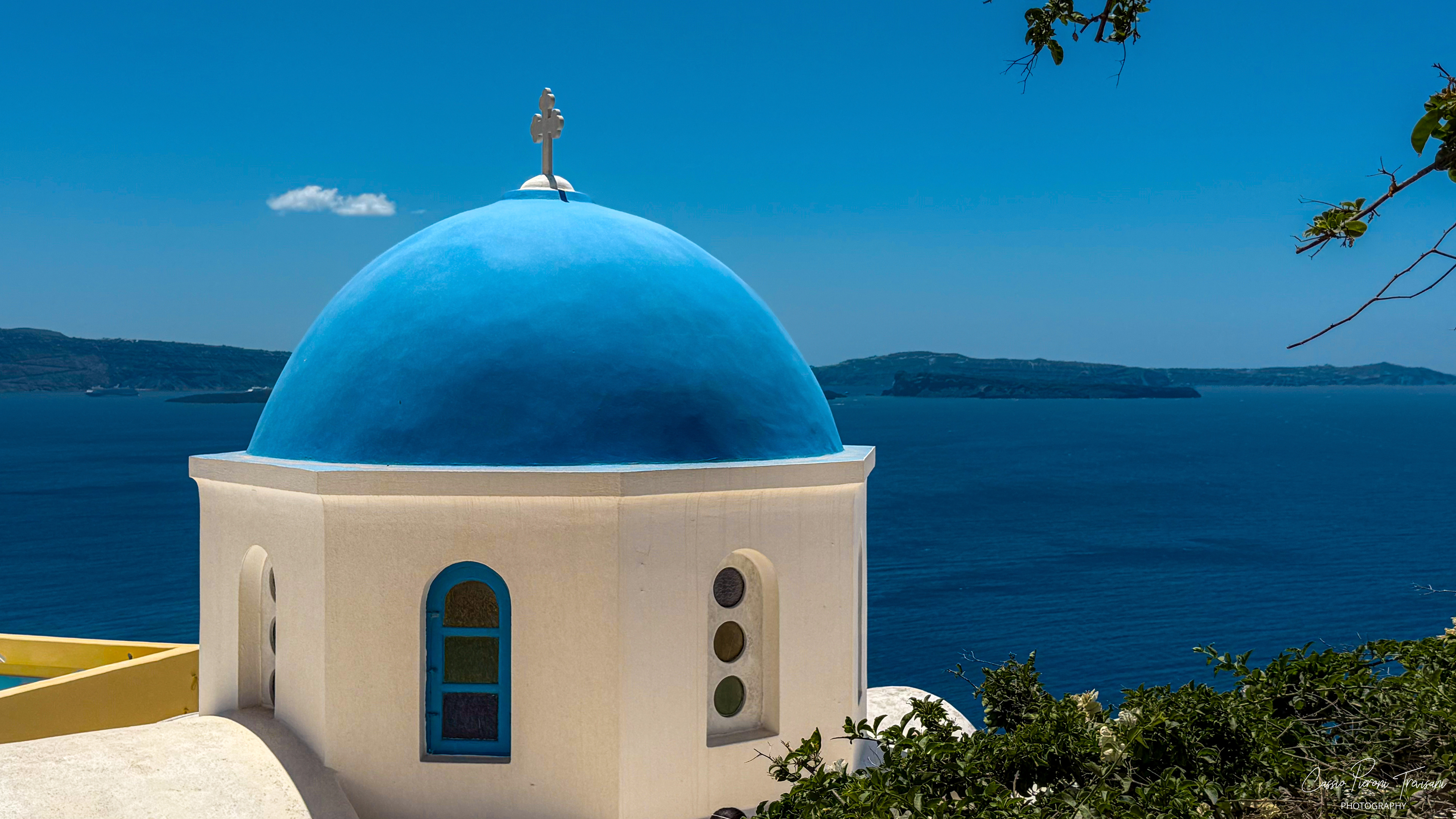 A classic blue-domed chapel overlooking the deep blue waters of the Santorini caldera.