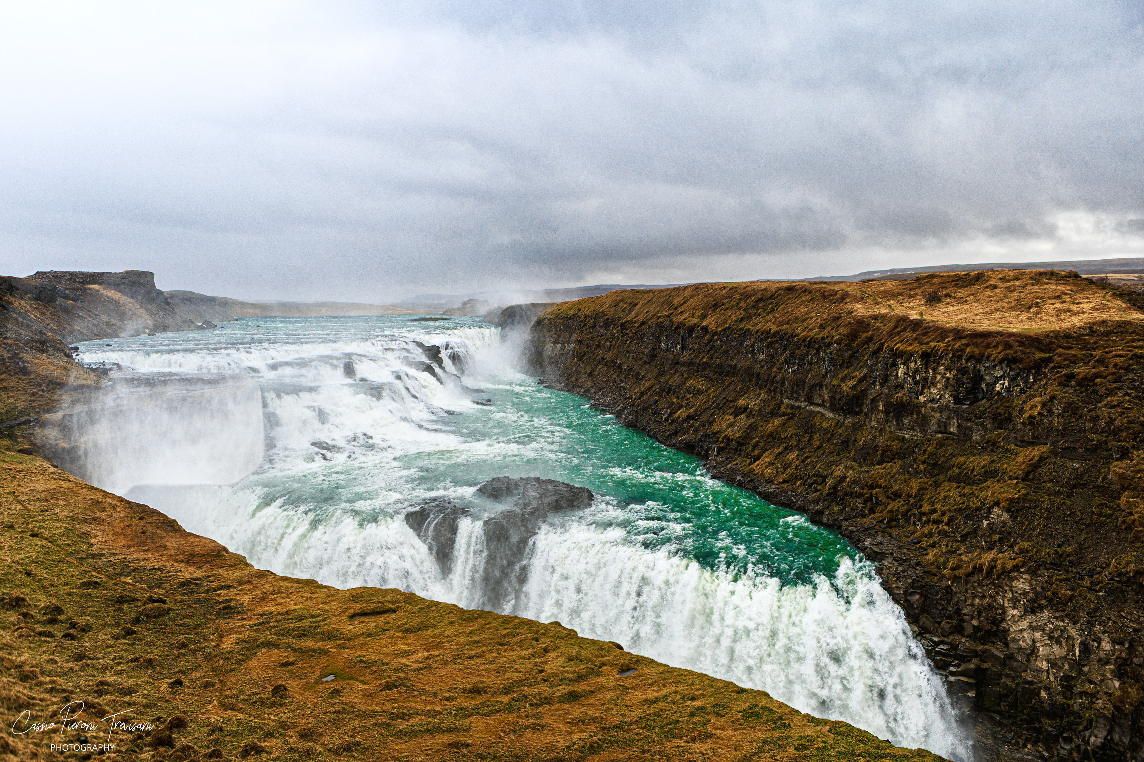 The Hvítá River plunges over the layered falls of Gullfoss, carving its way through dark rock and golden moss.