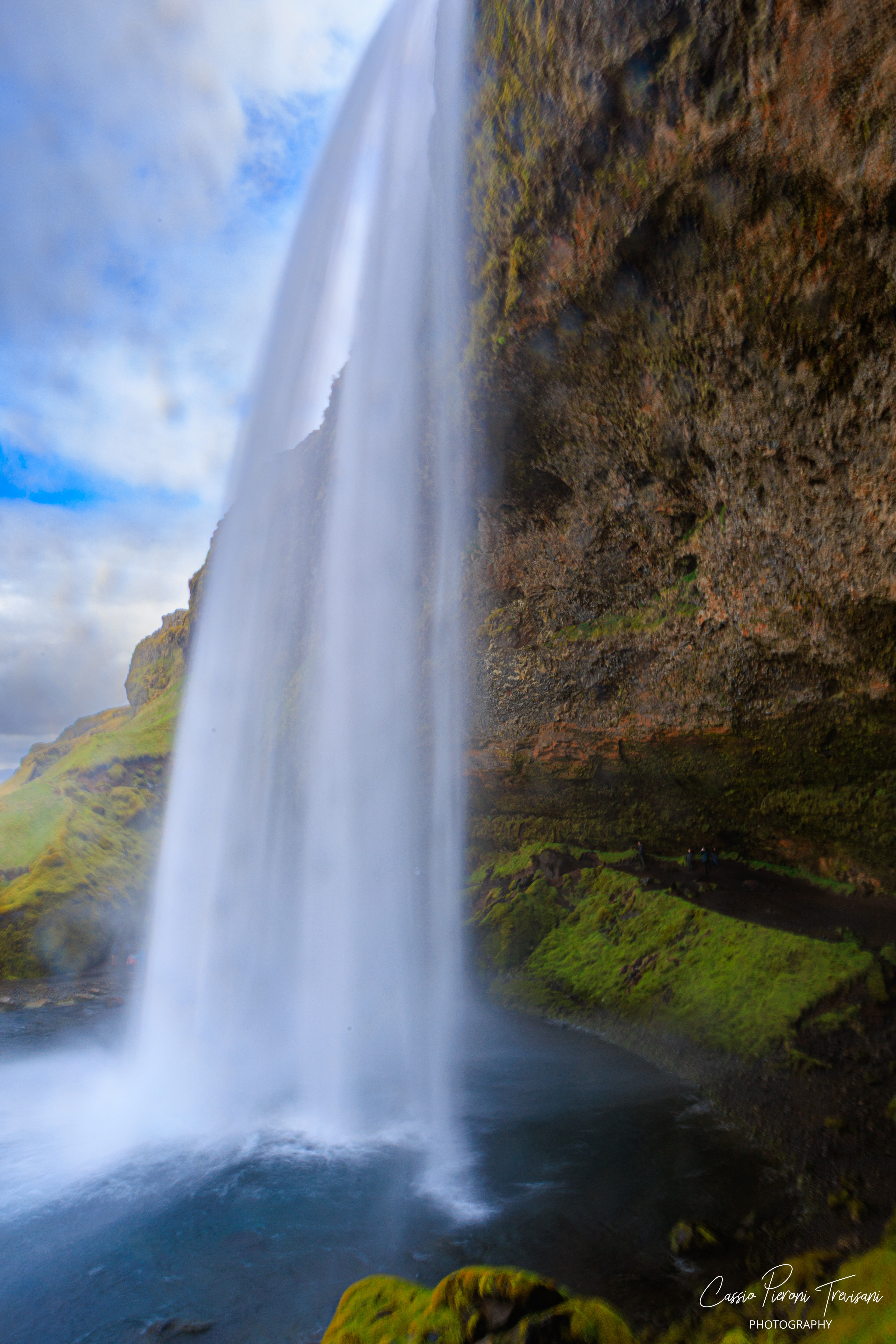 From behind Seljalandsfoss, the water becomes a soft curtain between the cliff face and the open Icelandic sky.