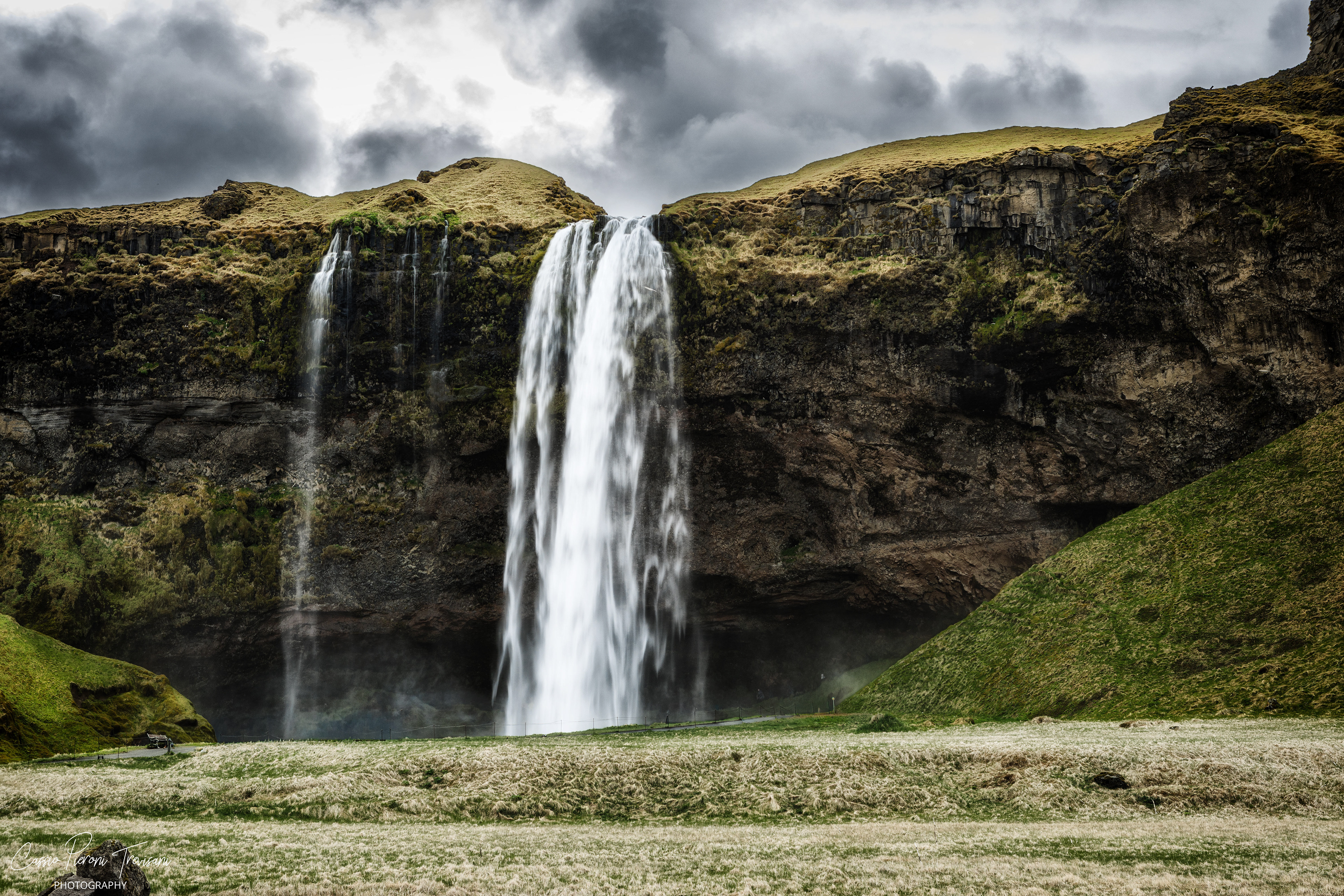 Seljalandsfoss drops from a moss-covered cliff beneath a heavy sky, filling the valley with mist and movement.
