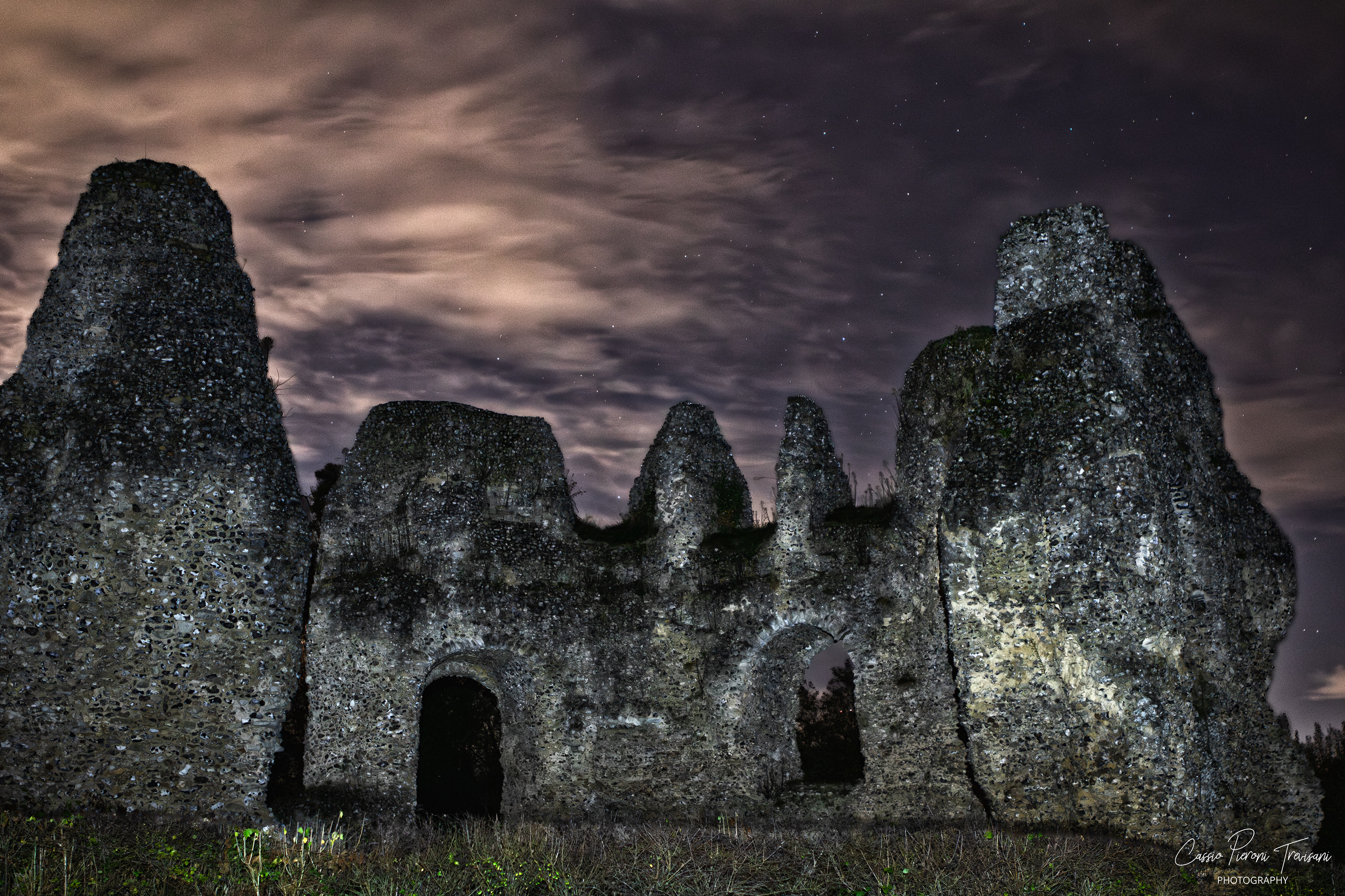 Wide nighttime shot of Odiham Castle’s jagged ruins against swirling illuminated clouds.