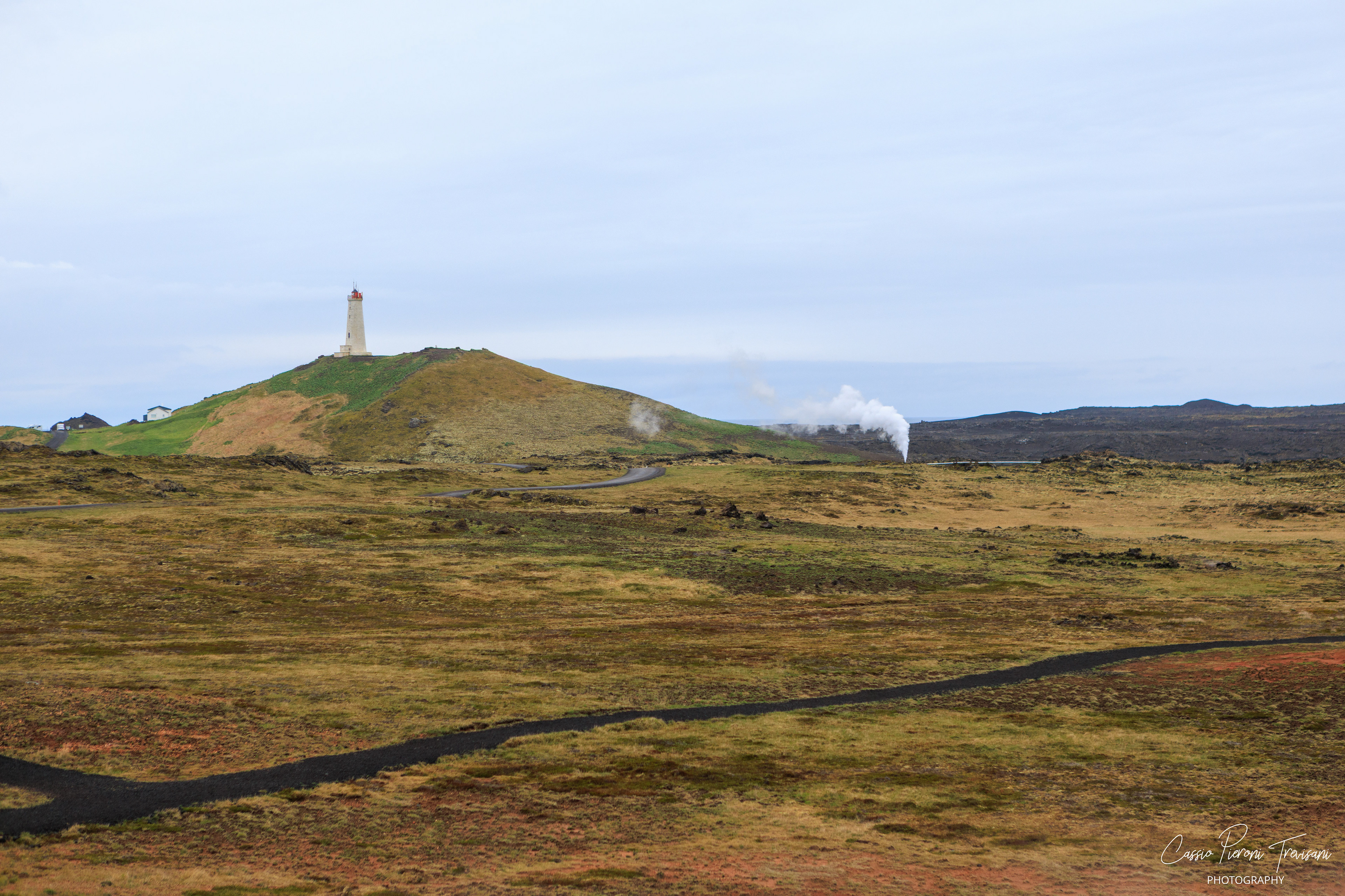 Reykjanesviti stands above the open geothermal plain, with steam rising in the distance across a landscape shaped by fire and sea.