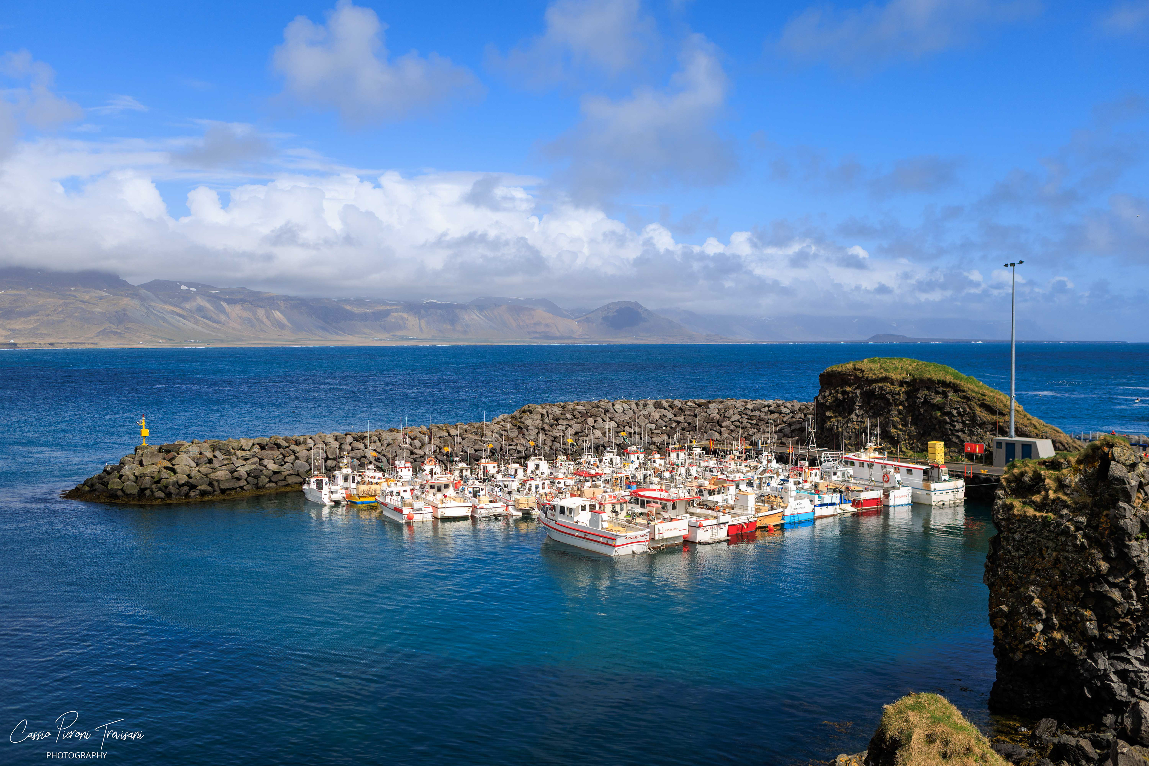 A colourful Arnarstapi Harbour rests between deep blue water and dark cliffs, showing a quieter coastal side of Icelandic life.
