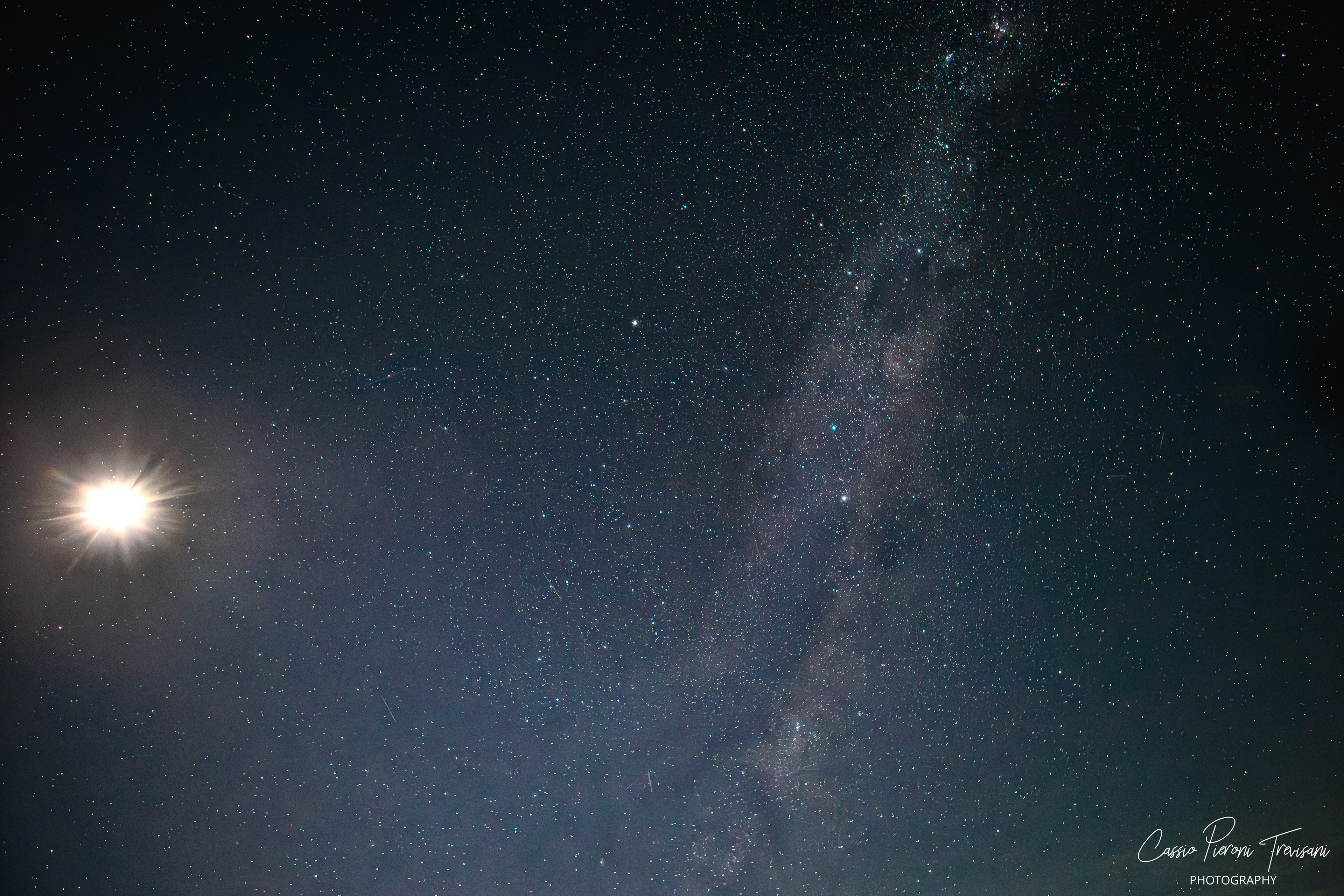 The Milky Way rises through a clear night sky as the Moon glows brightly on the horizon, illuminating countless stars above the countryside of southern Minas Gerais.