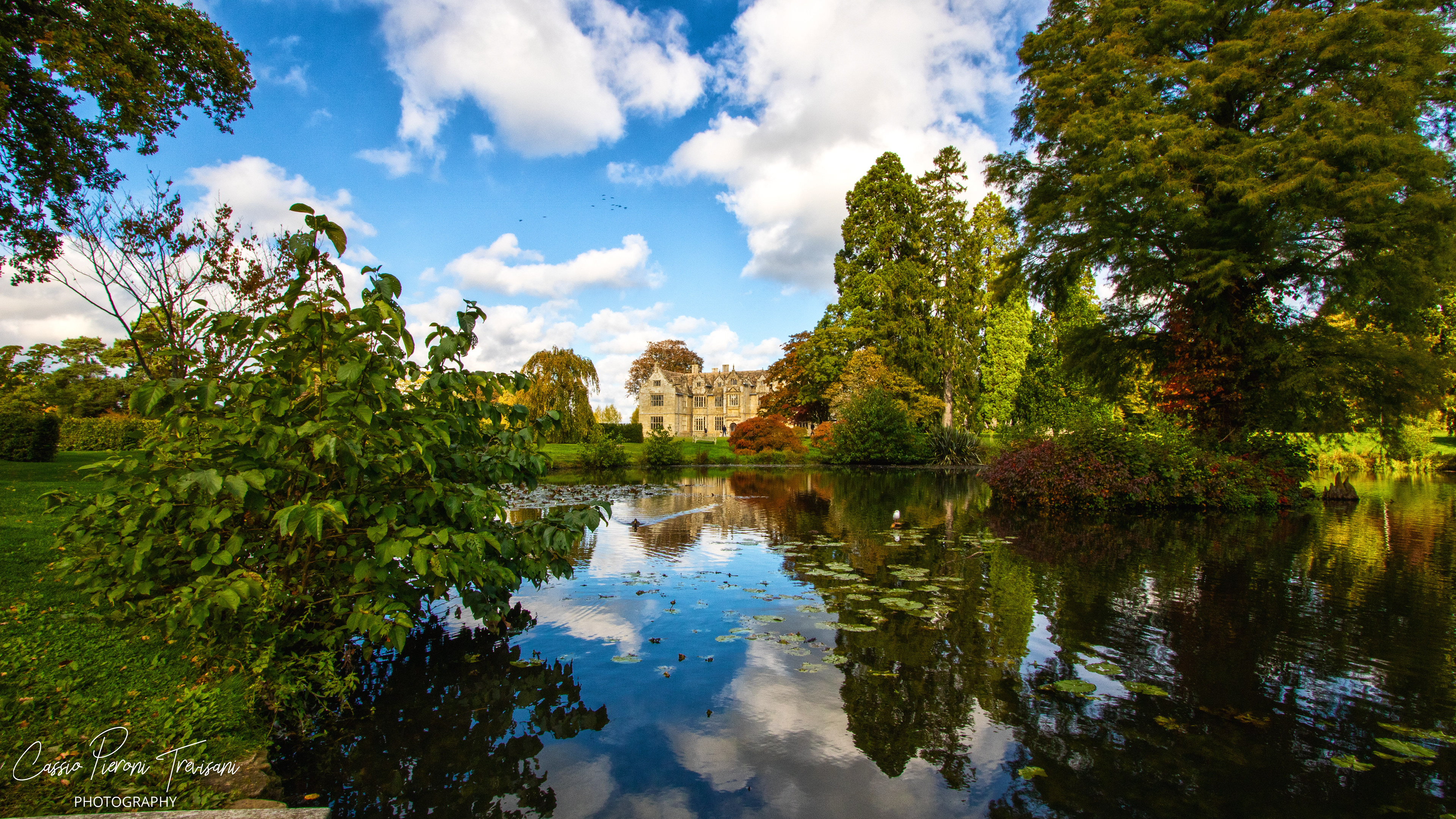 Wakehurst Place reflected across a peaceful garden lake.
