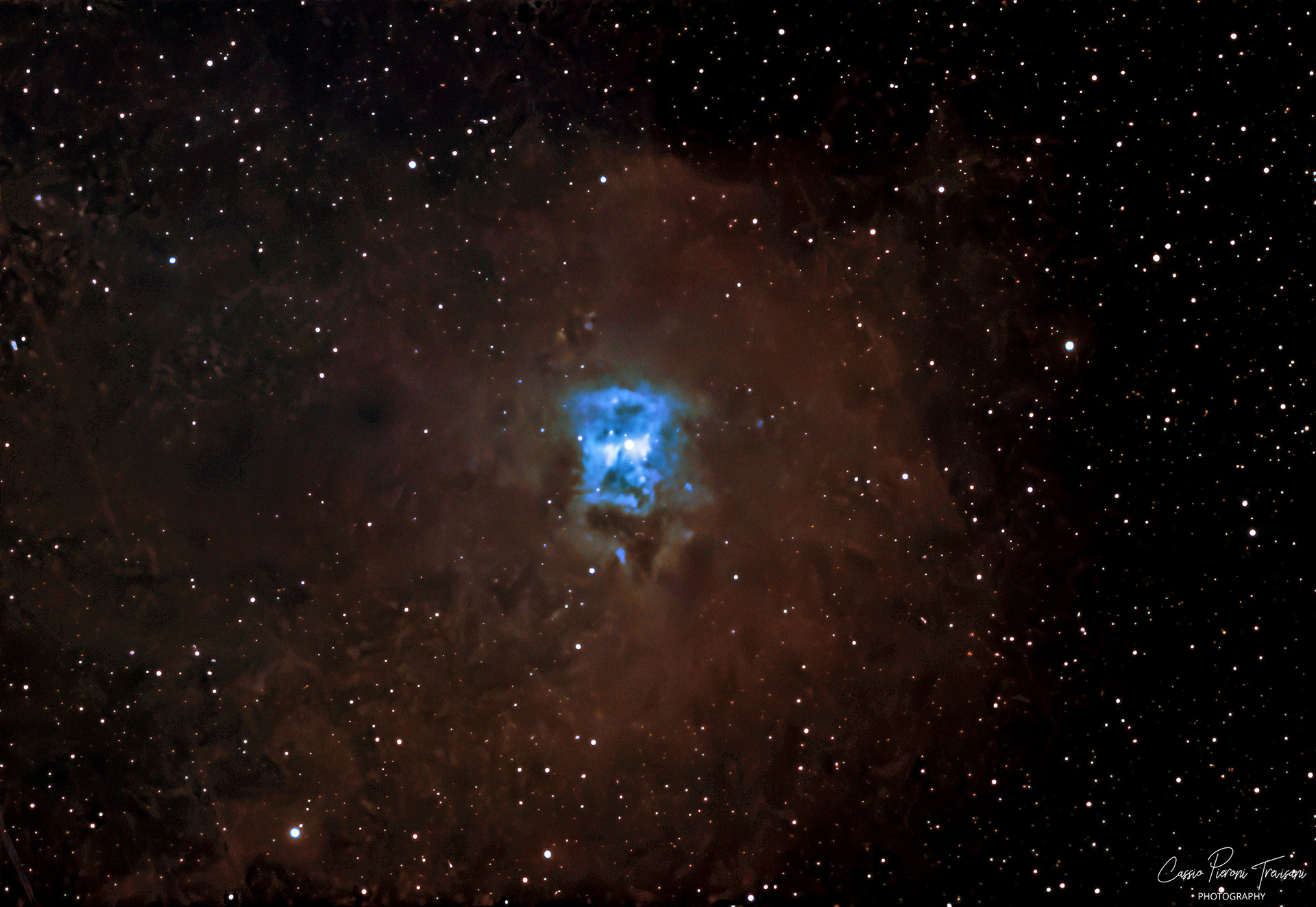 A deep-space image of the Iris Nebula showing a bright blue central region surrounded by dark, reddish-brown dust clouds, with numerous stars scattered across the background.