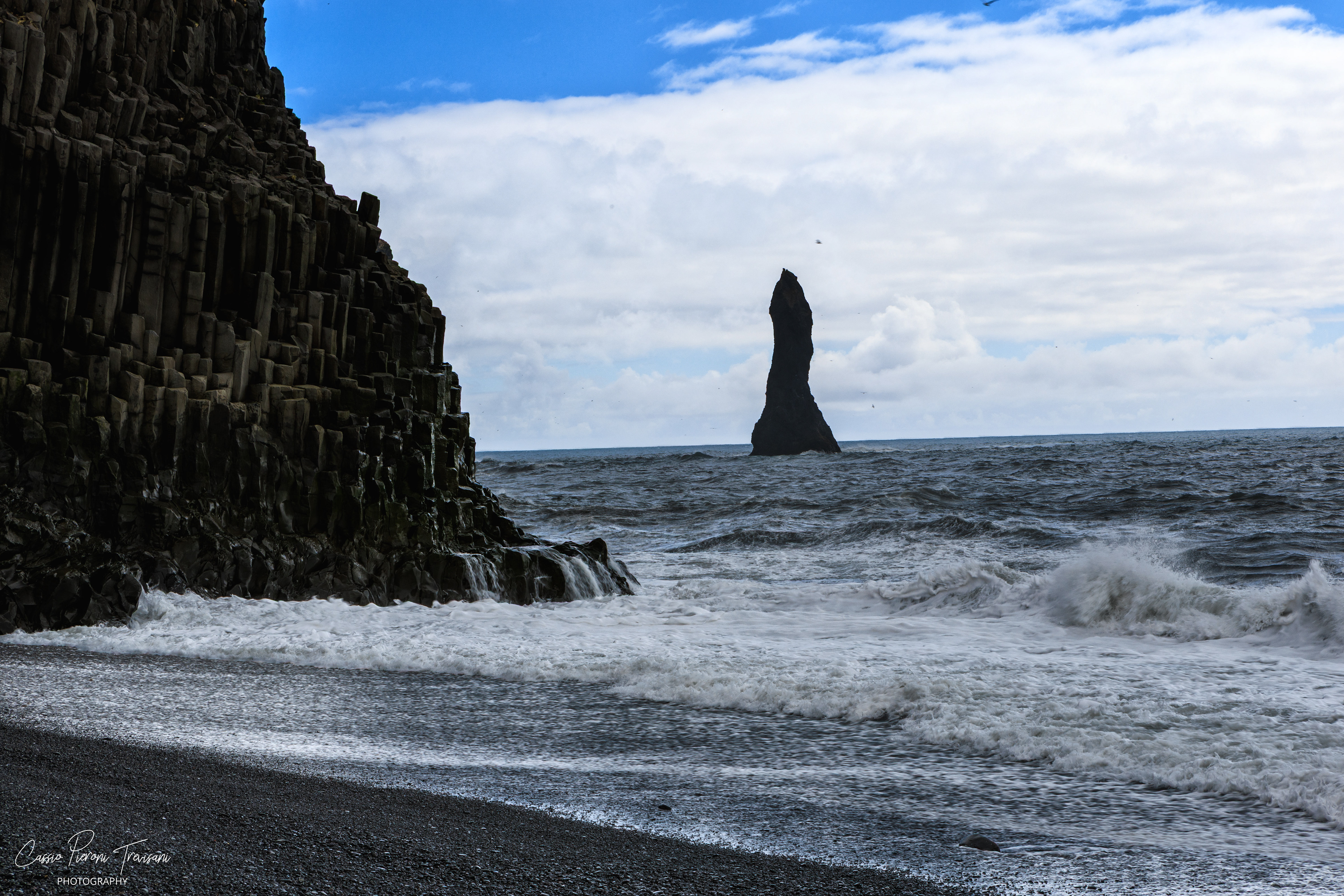 Basalt cliffs rise beside the Atlantic as Reynisdrangar stands offshore, surrounded by restless waves and seabirds.