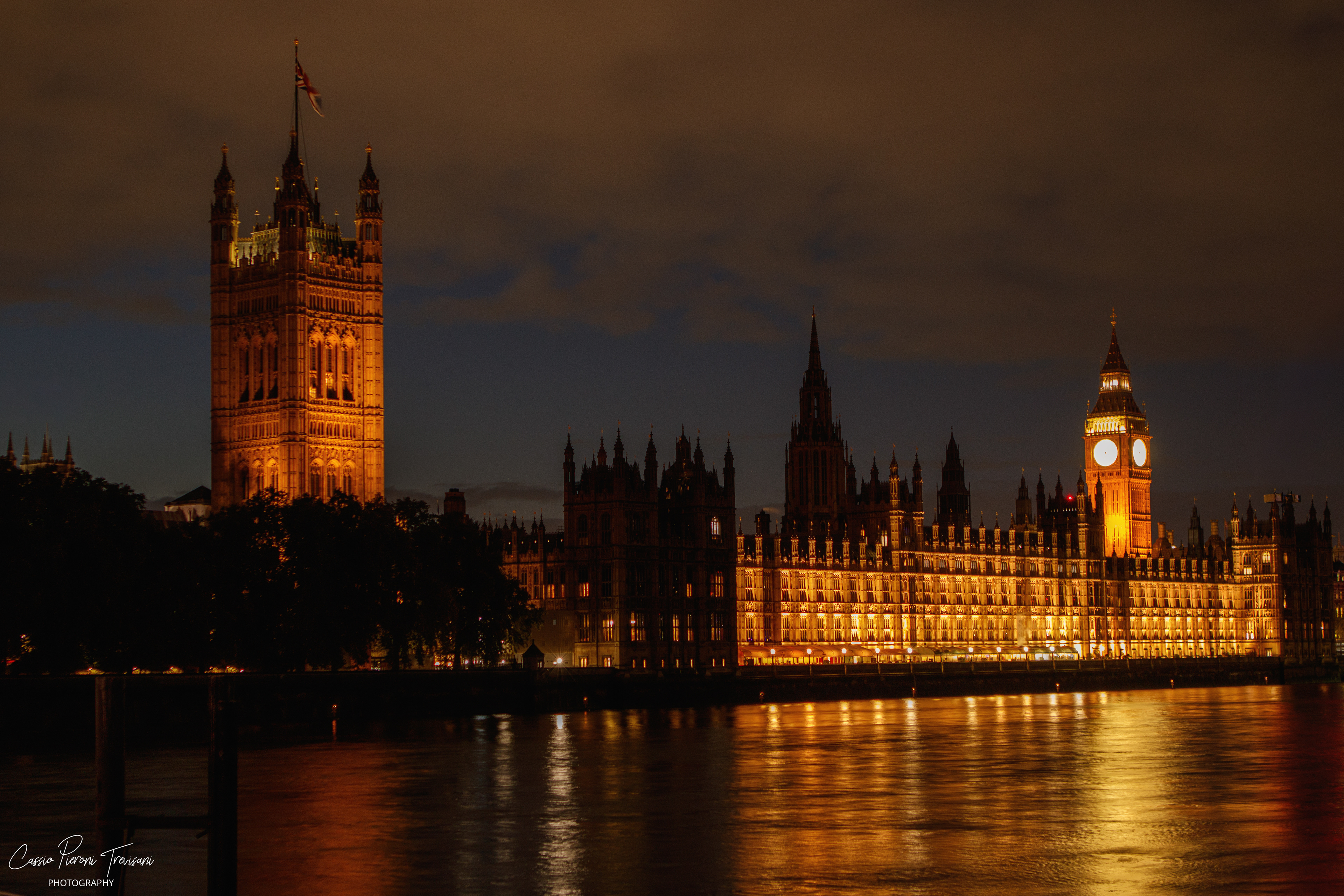 Under a restless London sky, the Palace of Westminster radiates in gold while Big Ben marks time beside the quiet flow of the Thames.