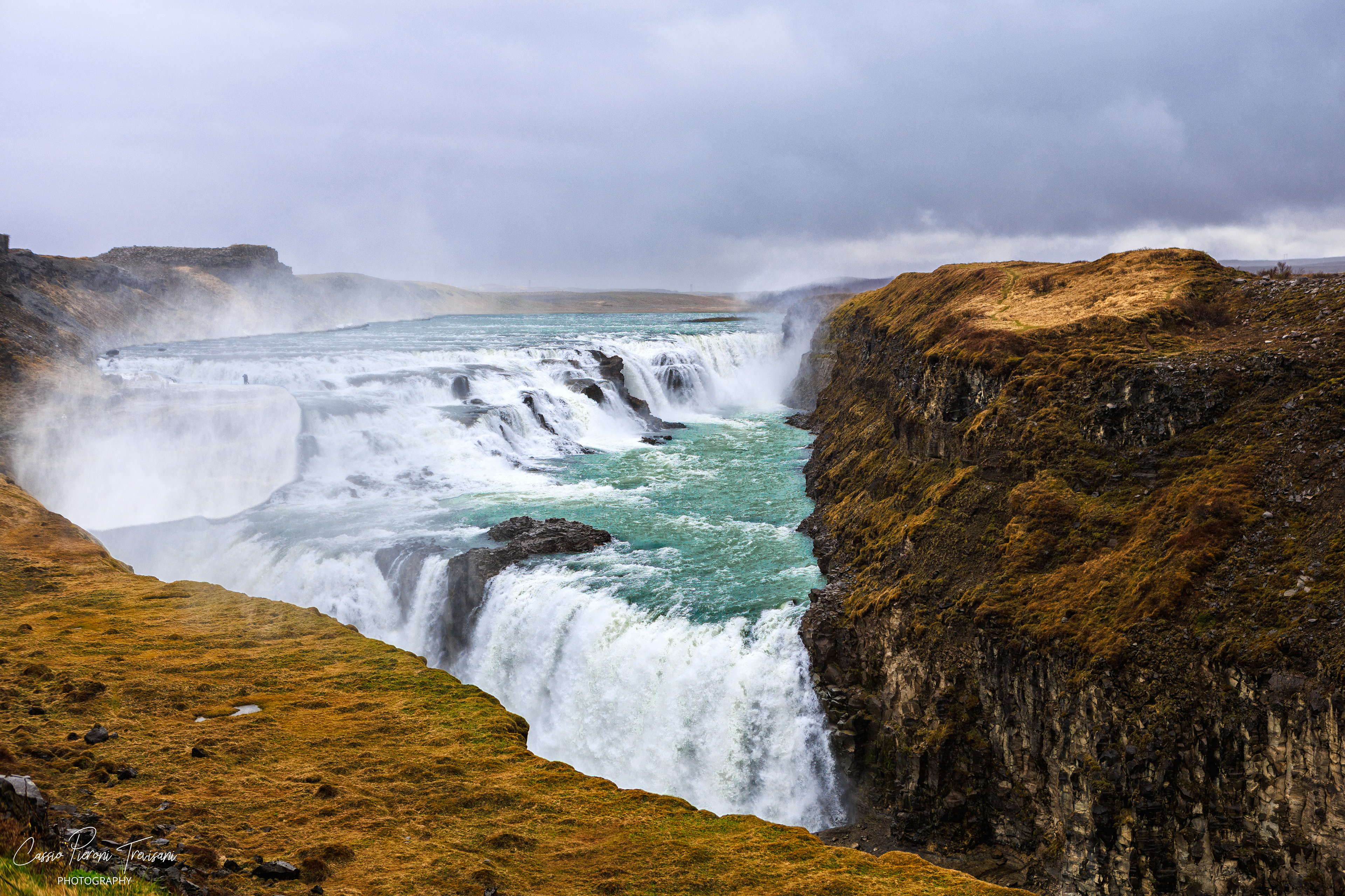Gullfoss thunders through the canyon, sending glacial water and mist into the cold air beneath a heavy Icelandic sky.