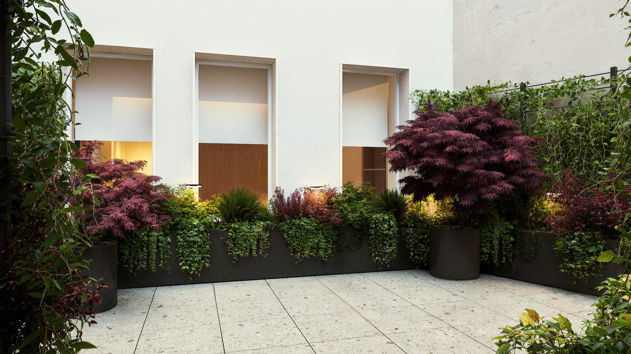 Courtyard with a relaxing atmosphere featuring ceppo di grè stone floor and lush greenery inside black metal planters – Yume Visual
