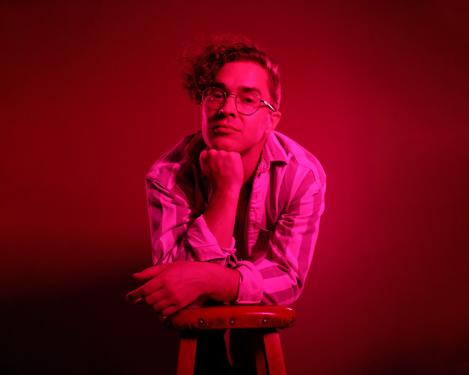 A photo of Landon Maxwell leaning on a chair in strong pink and red lighting