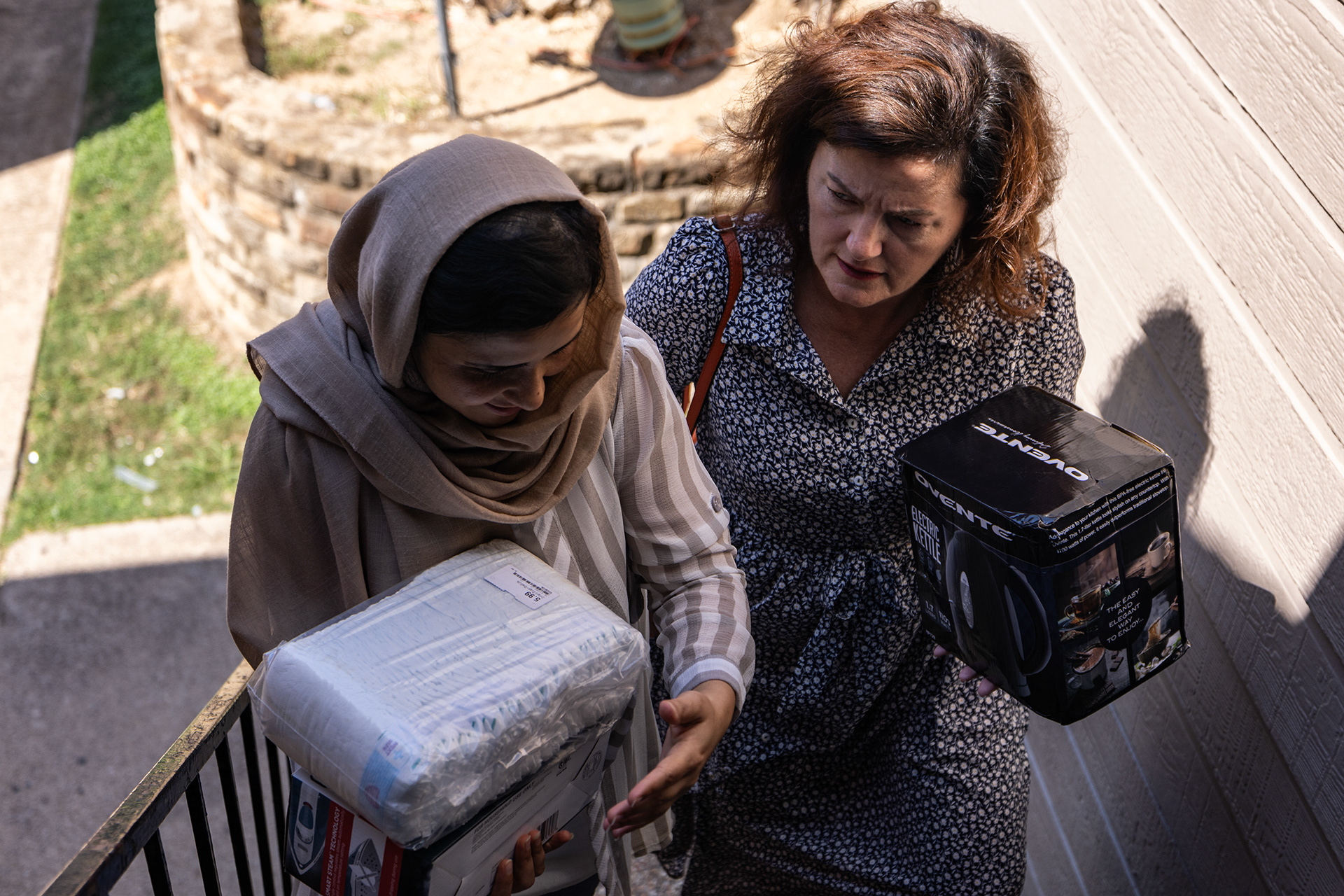 Nilofar Safi, left, helps Angie Kraus carry diapers, an iron and a tea kettle up to Aziza’s apartment in Fort Worth on Wednesday, Sept. 27, 2023.