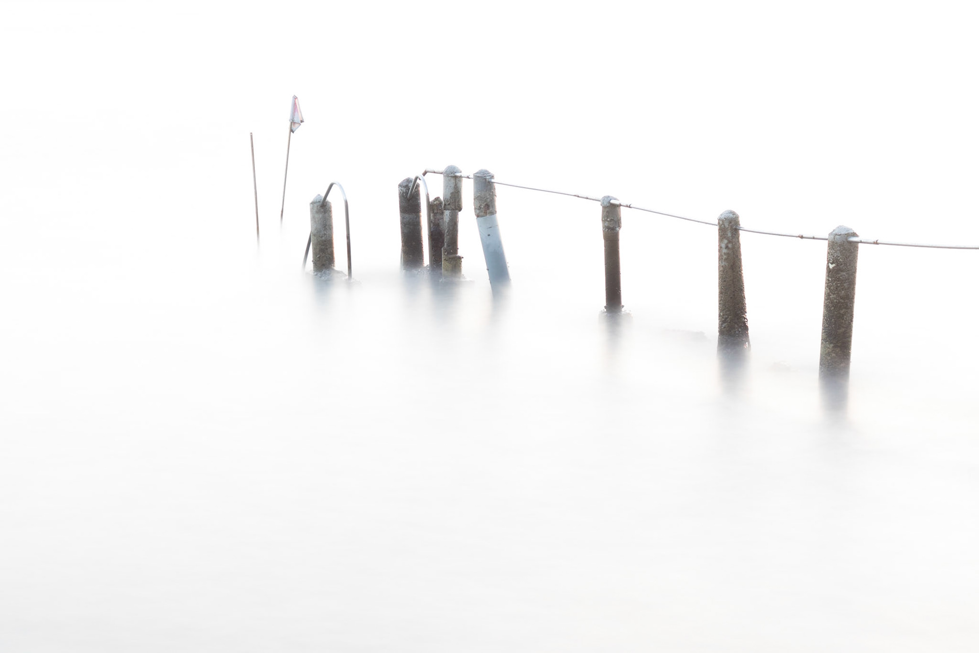 Old damaged concrete and metal pier partially submerged with a silky  smooth sea.  Long exposure photograph.