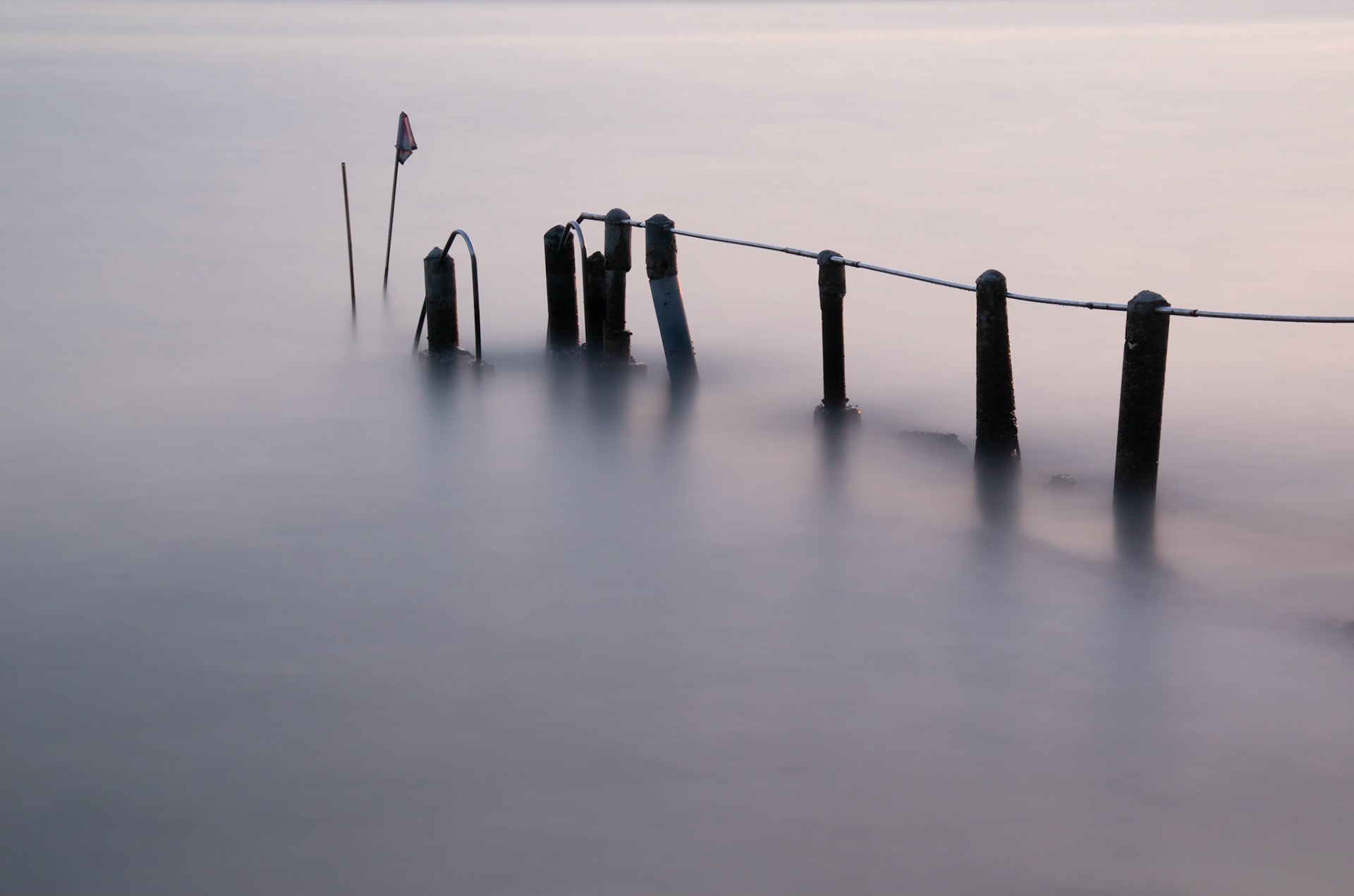 Old damaged concrete and metal pier partially submerged with a silky  smooth sea.  Long exposure photograph.
