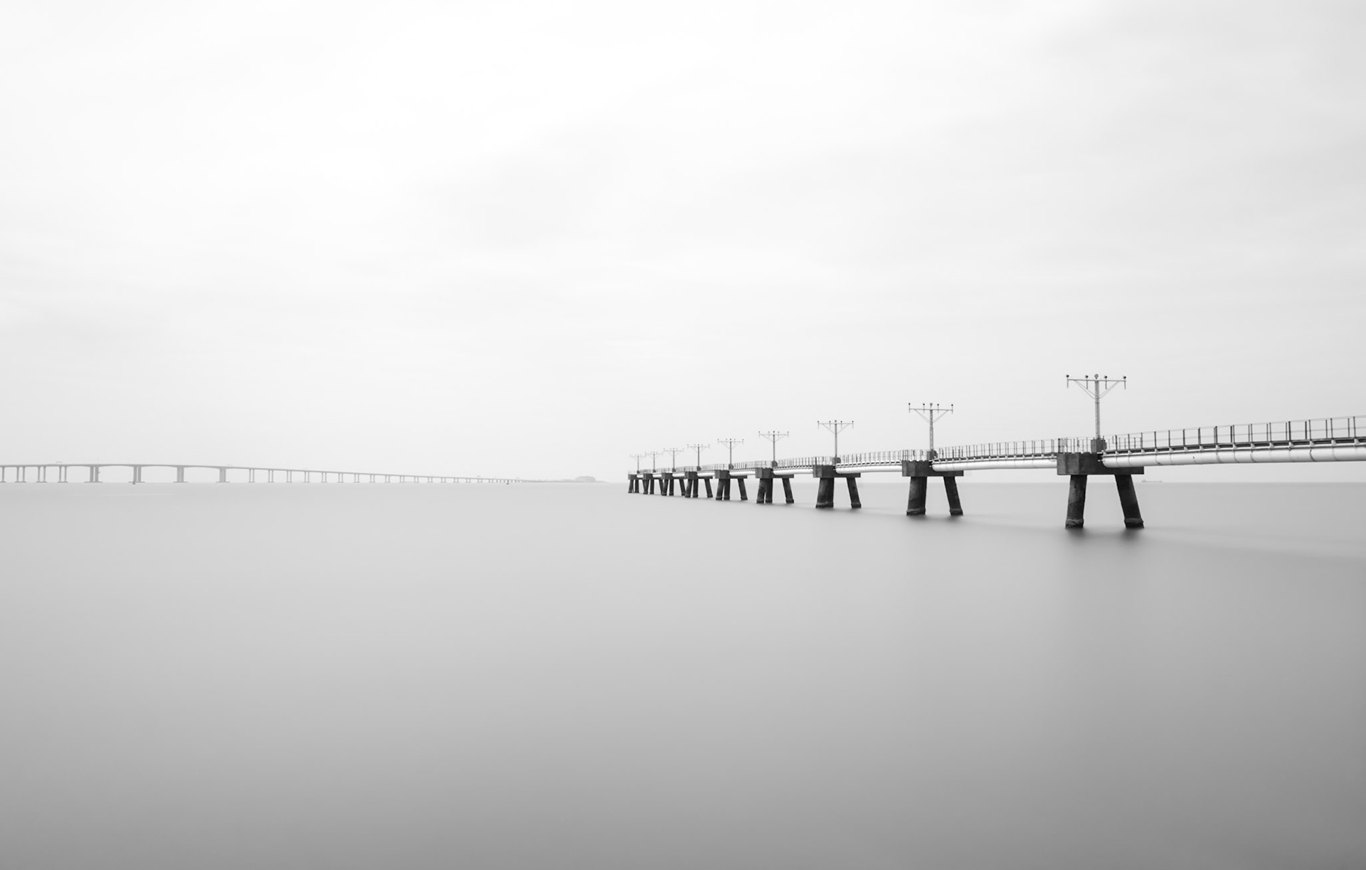 Pier with landing lights at Hong Kong airport extends out into the sea.  Long exposure gives a smooth sea