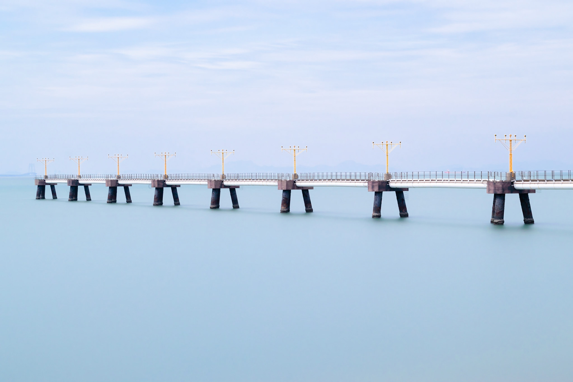Pier with landing lights at Hong Kong airport extends out into the sea.  Long exposure gives a smooth sea