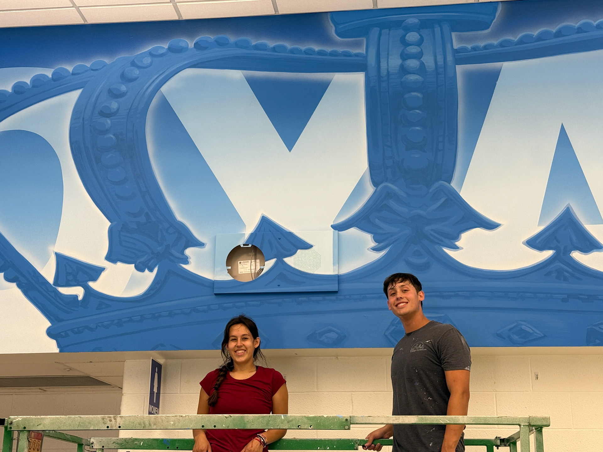 employees on scissor lift painting, crown visible behind them