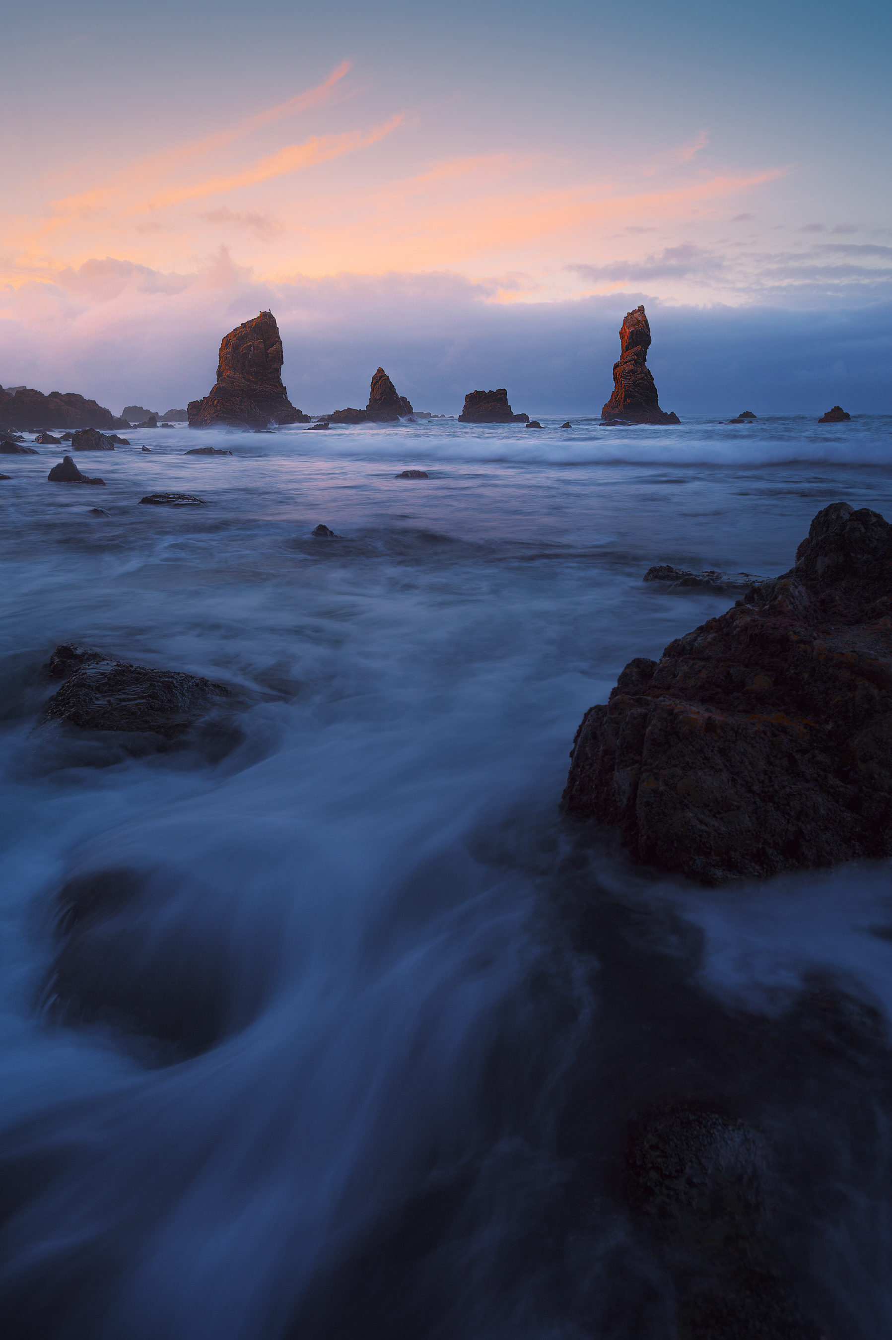 Atardecer en la costa de valdés, asturias, las olas golpean con fuerza las rocas y el cielo se colorea