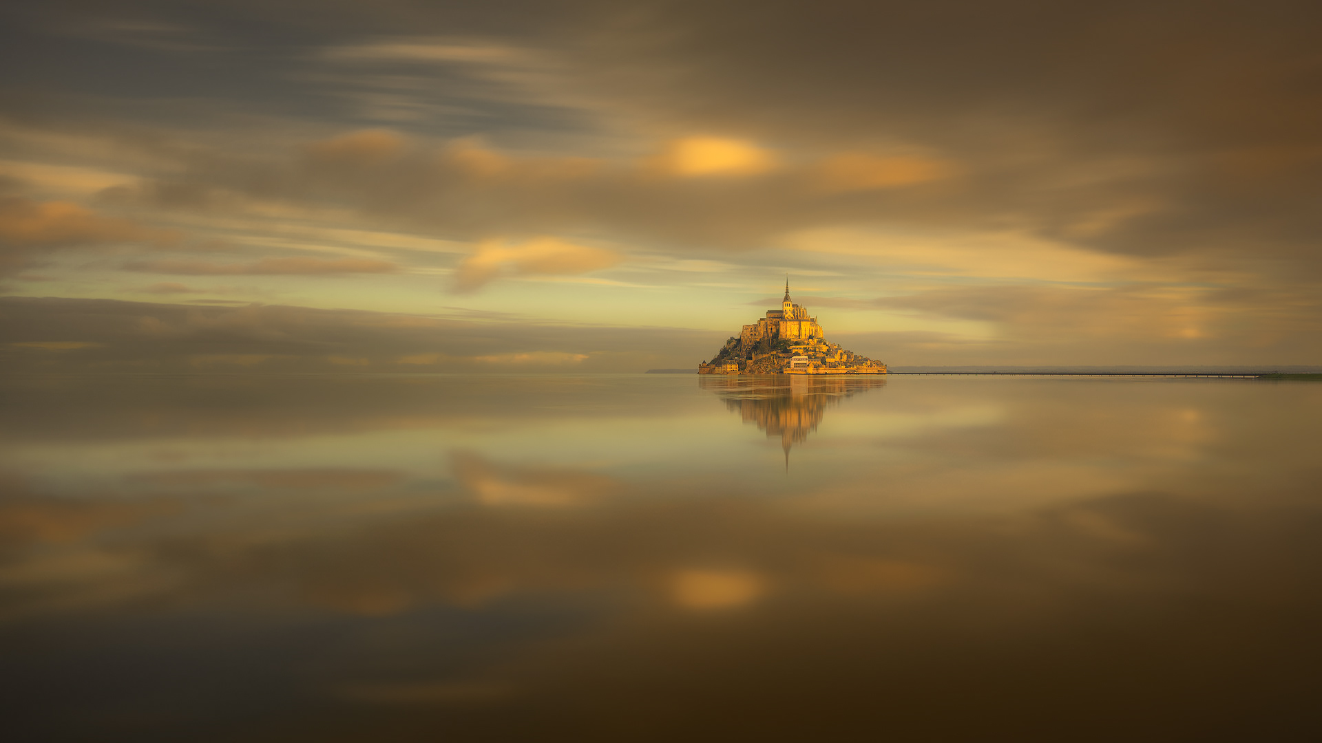 Fotografía del Mont Saint-Michel durante las grandes mareas, un fenómeno natural espectacular. La imagen muestra la icónica abadía rodeada por el agua del Atlántico al atardecer, con reflejos dorados en el agua y detalles arquitectónicos nítidos. Ideal para los amantes de la fotografía de paisajes, larga exposición y destinos turísticos únicos