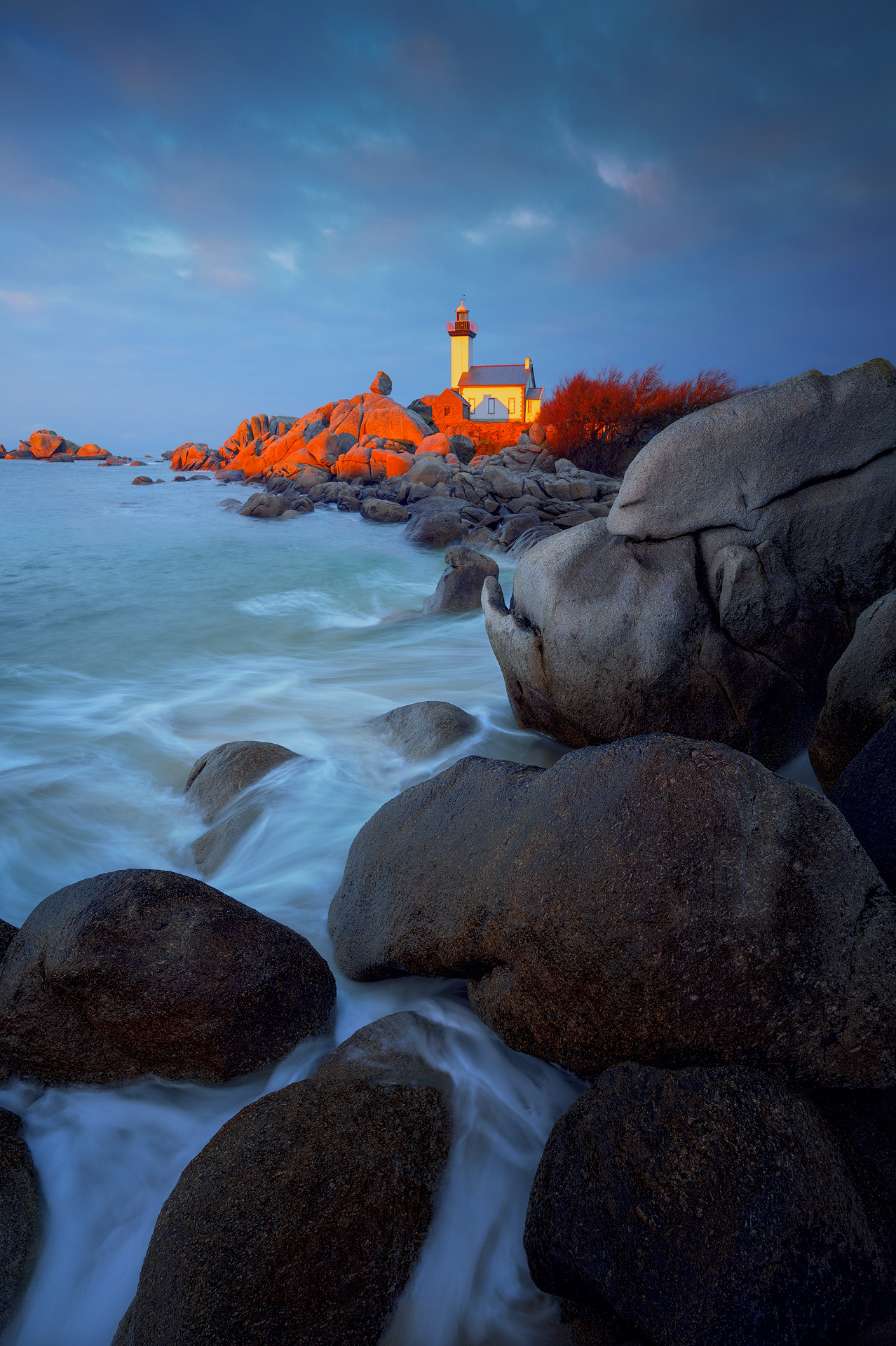sin la tecnica ¡Por supuesto! Aquí tienes una descripción alternativa de la foto, sin la técnica fotográfica:  Descripción de la imagen:  Una fotografía del Faro de Pontusval, situado en la costa de Plounéour-Brignogan-Plages en Bretaña, Francia. El faro es blanco y tiene forma cilíndrica, con una linterna en la parte superior. Se encuentra en una plataforma rocosa que sobresale en el océano Atlántico. El cielo está pintado con los tonos cálidos del atardecer, mezclando colores dorados y rosados. En primer plano, las olas del mar golpean suavemente las rocas y las playas de arena que rodean el faro.