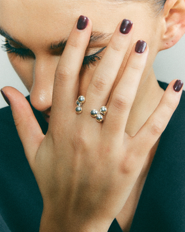 Detal twarzy i dłoni kobiety z bordowym manicure oraz srebrną biżuterią