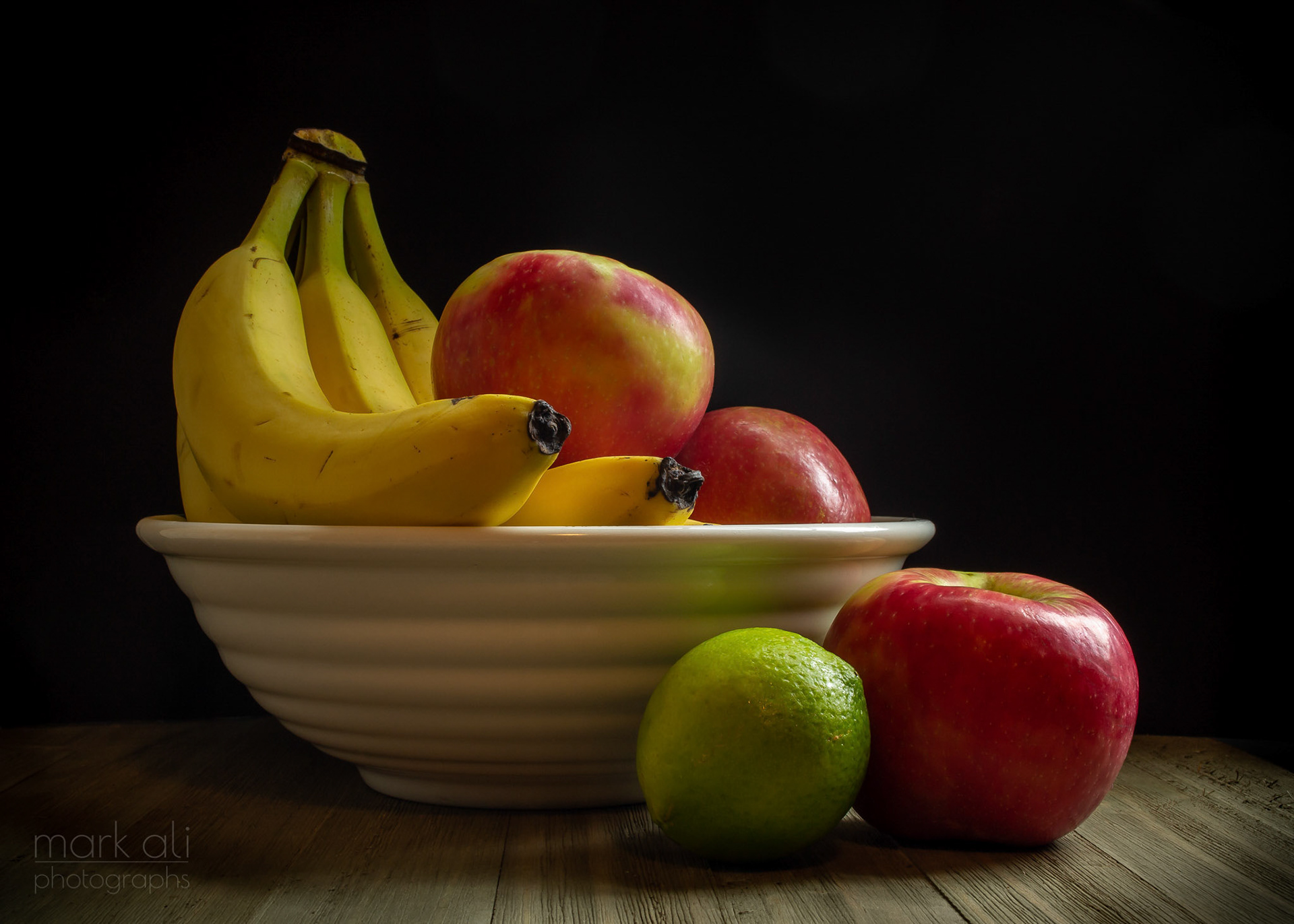 A bowl of fruit, with a green lime on the side.