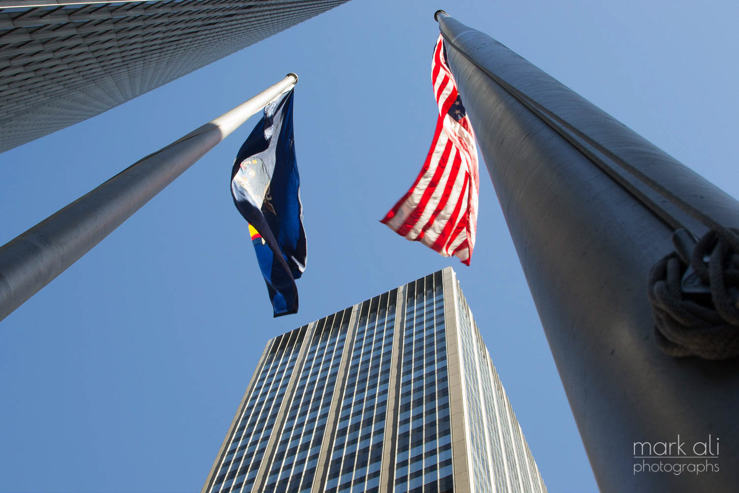 Looking up at a tall Manhattan building and flag poles.