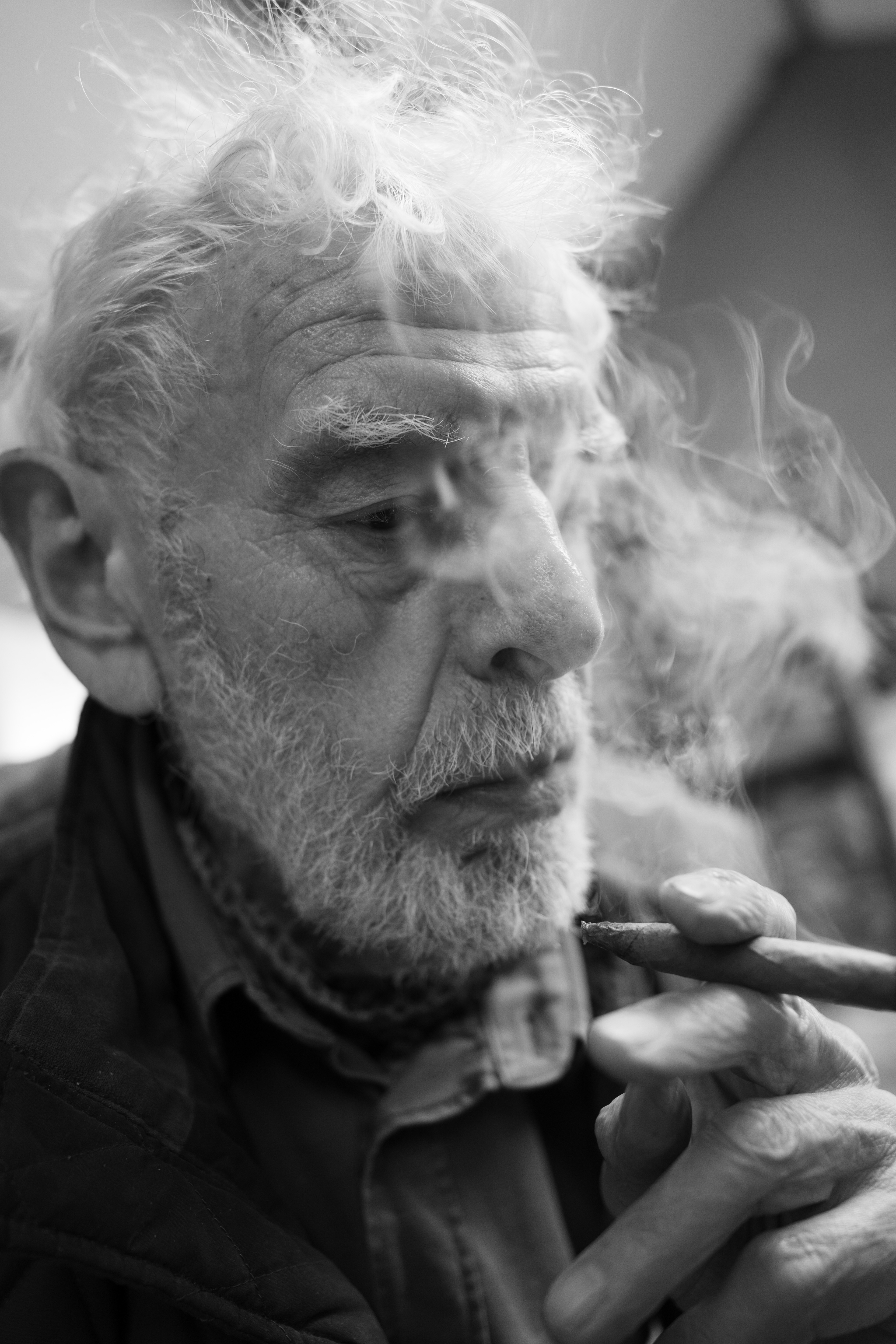 Mike Knowles (June 2025) - Artist Mike Knowles pictured here in a relaxed mood enjoying a contemplative smoke break in his art studio in Sir Fon (Anglesey) North Wales. Mike is Professor Emeritus of Liverpool University Fine Art Department - he is a fine artist in his own right, and paints mostly landscapes from his North Wales studio. Even in his mid eighties , he is a prolific painter of landscapes