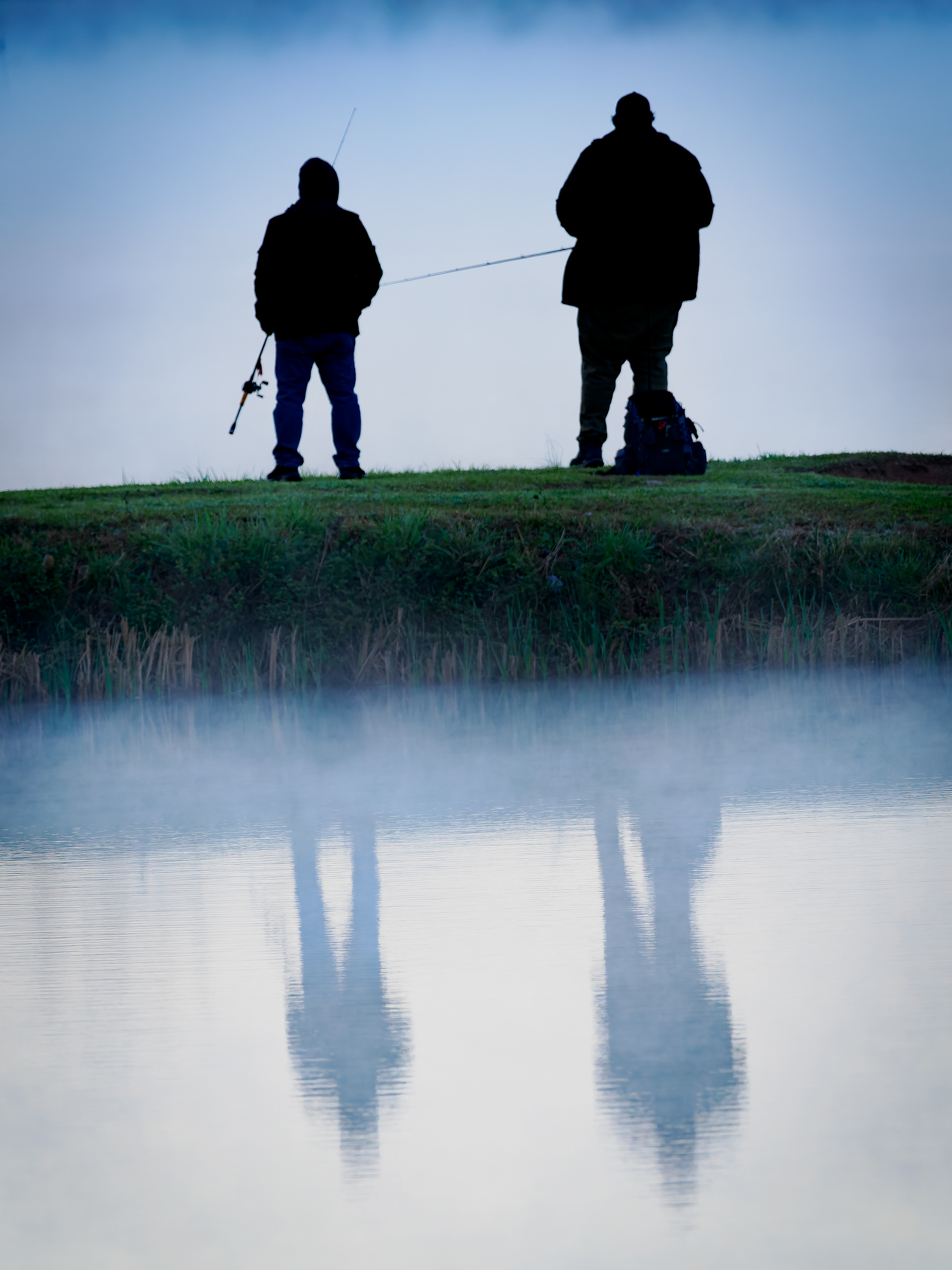 Man and boy fishing at sunrise.  With reflections in water.  Jefferson Lake in Jefferson Georgia.