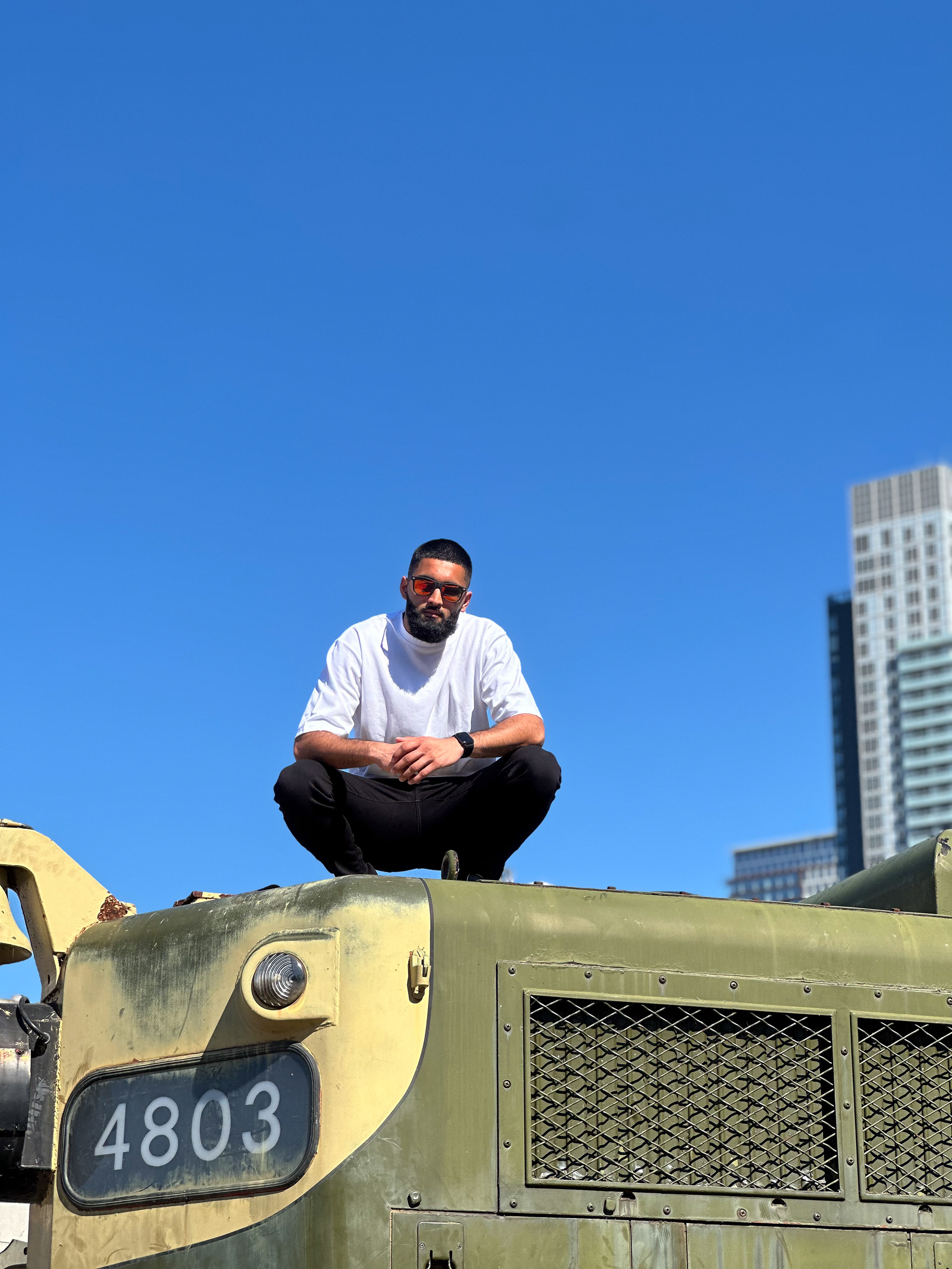 Muhammad Abbasi | Lifestyle | White oversized t-shirt, black jeans, colorful sneakers, sitting on top of vintage train engine numbered 4803