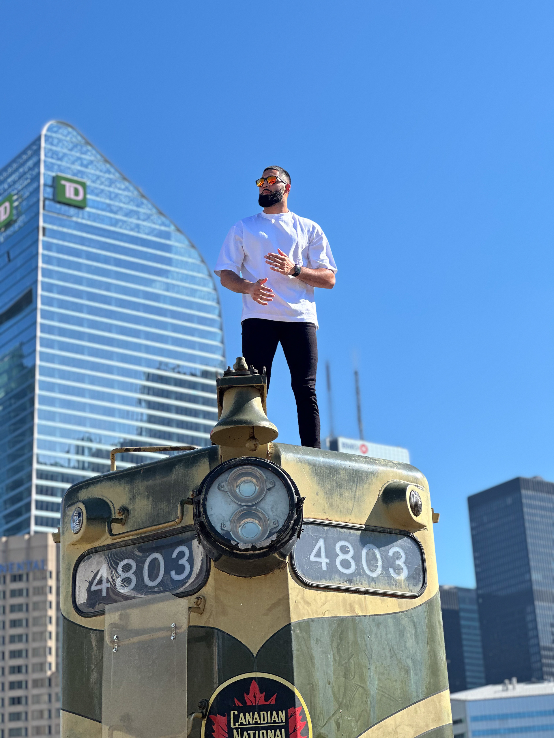 Muhammad Abbasi | Lifestyle | White oversized t-shirt, black jeans, colorful sneakers, looking ahead while standing on vintage train engine