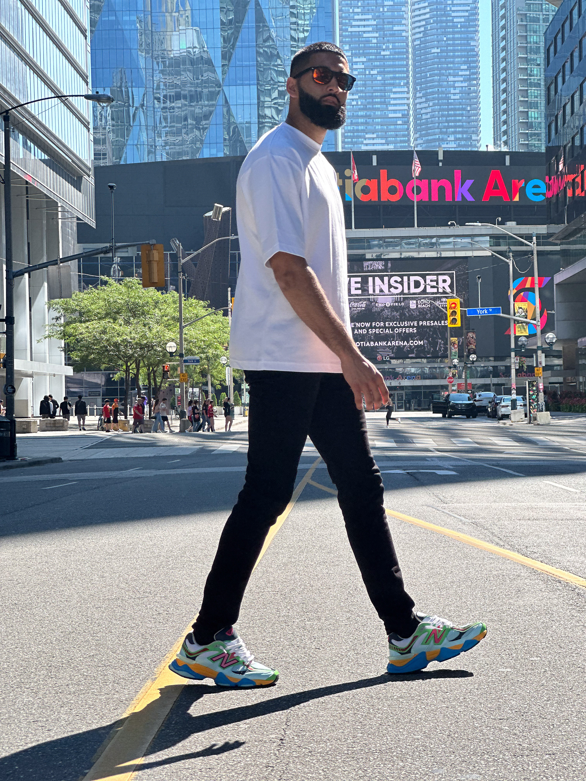 Muhammad Abbasi | Lifestyle | White oversized t-shirt, black jeans, colorful sneakers, walking across Toronto street with Scotiabank Arena in background