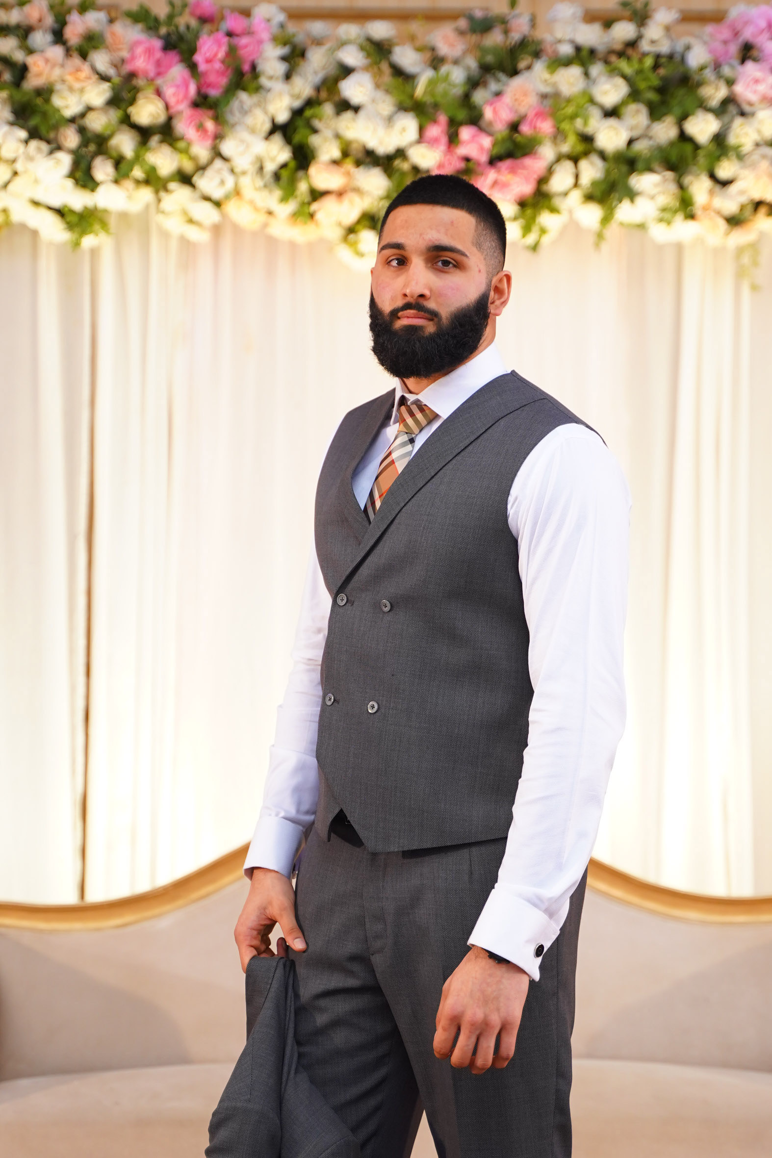 Muhammad Abbasi | Formal Wear | Charcoal vest and trousers with striped tie, looking into distance holding jacket