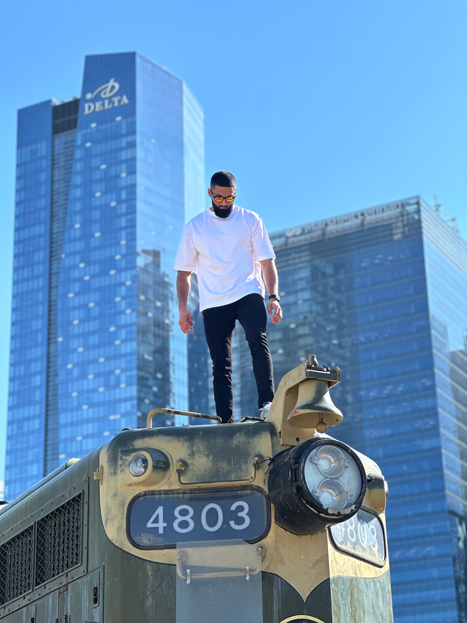 Muhammad Abbasi | Lifestyle | White oversized t-shirt, black jeans, colorful sneakers, looking down while standing on vintage train engine