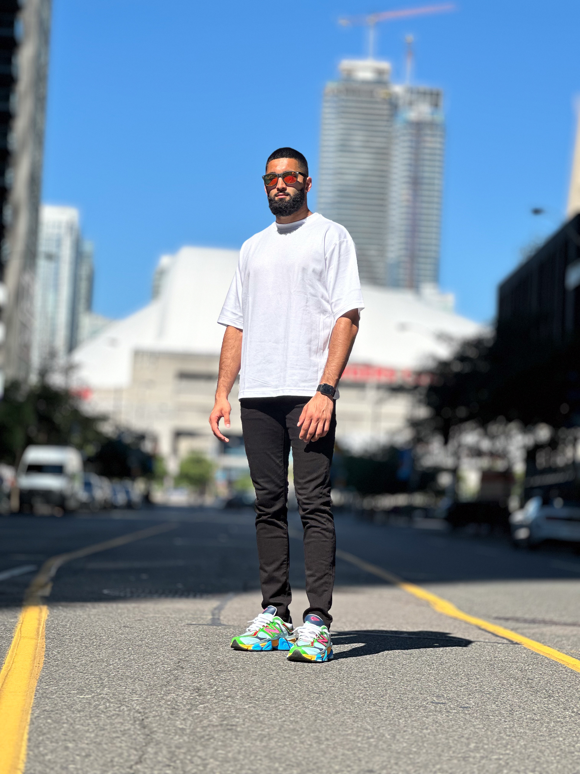 Muhammad Abbasi | Lifestyle | White oversized t-shirt, black jeans, colorful sneakers, standing in the middle of the road with Toronto skyline in background