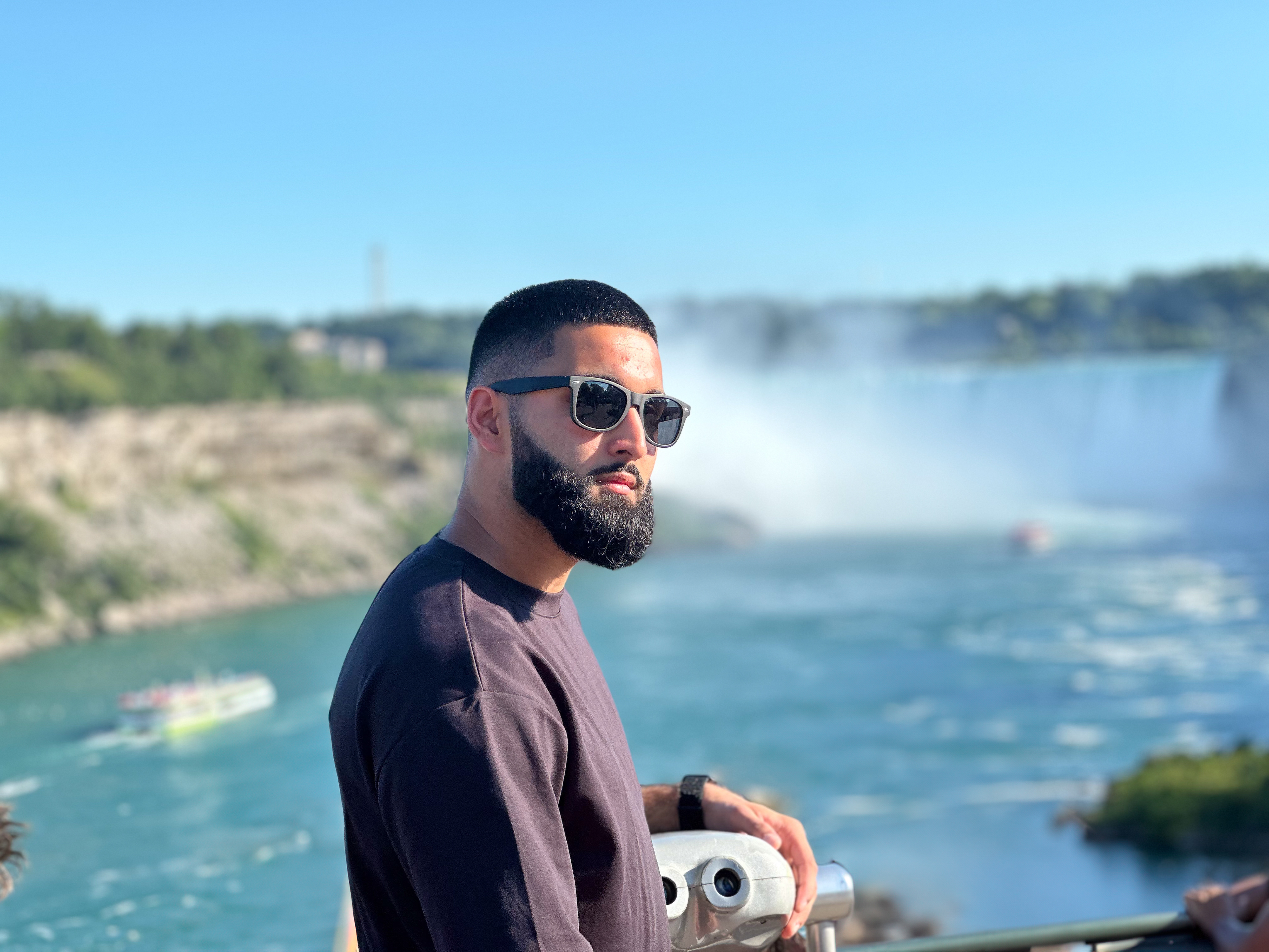 Muhammad Abbasi | Lifestyle | Black t-shirt, light blue jeans, black sneakers, side close-up by railing with falls in background