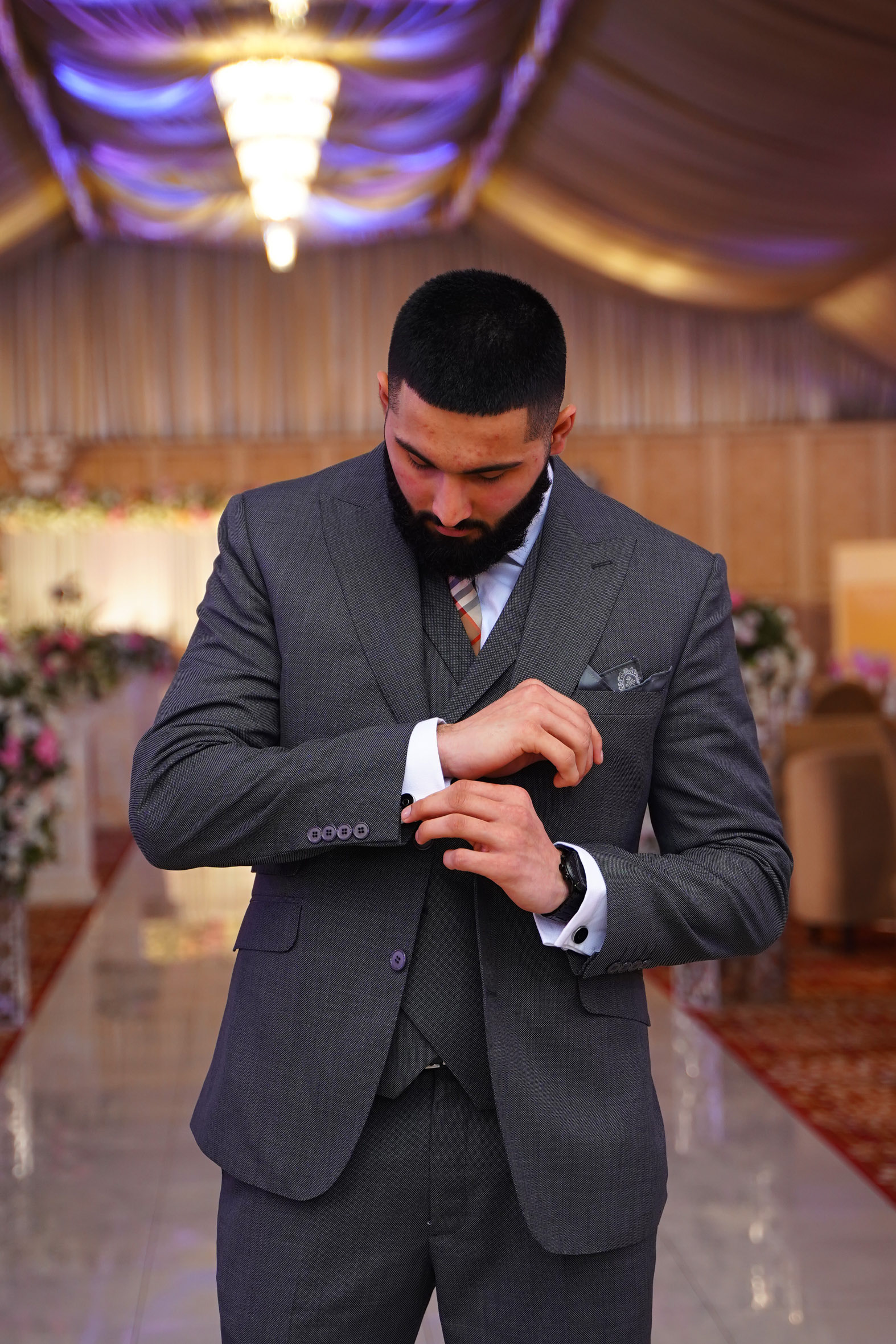 Muhammad Abbasi | Formal Wear | Charcoal three-piece suit with striped tie, adjusting cufflinks