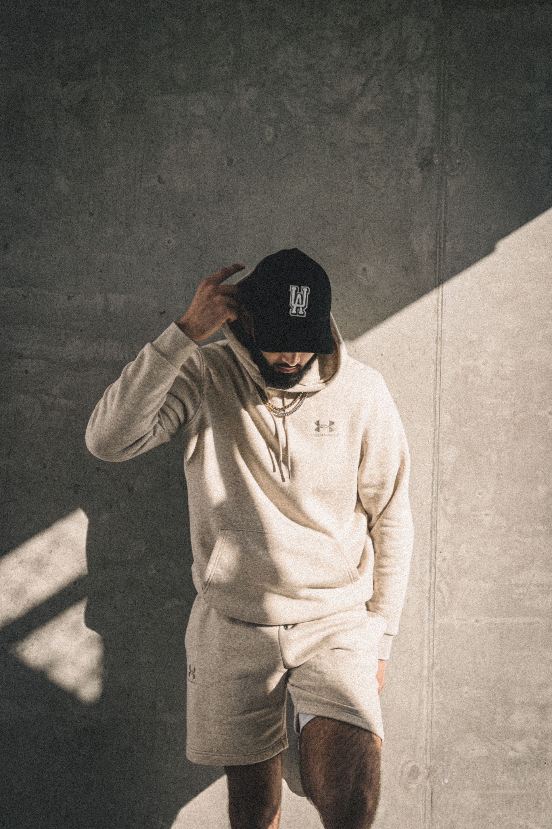Muhammad Abbasi | Under Armour | ICON Fleece Hoodie | Adjusting cap against a concrete wall
