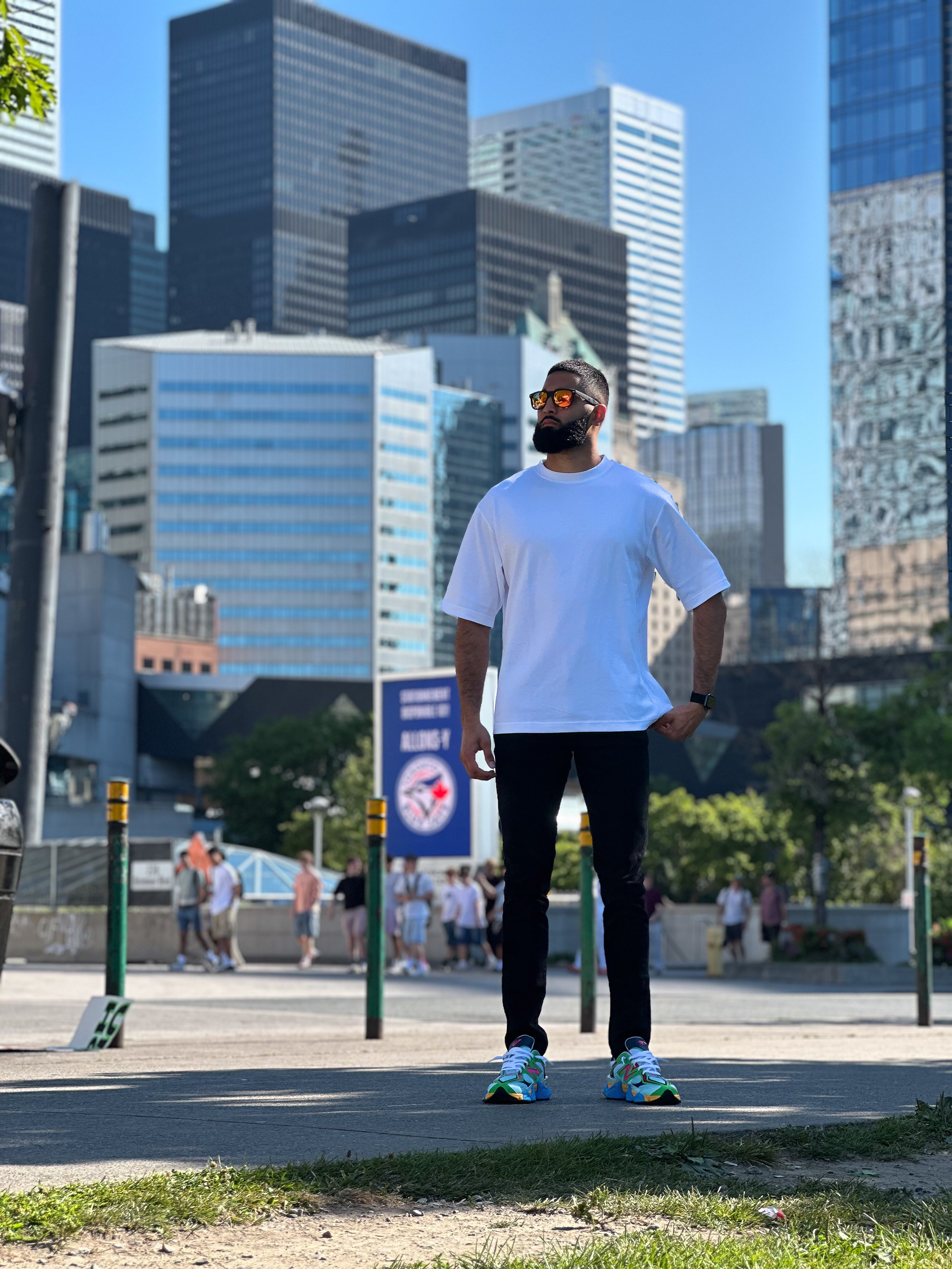 Muhammad Abbasi | Lifestyle | White oversized t-shirt, black jeans, colorful sneakers, standing in downtown Toronto with skyscrapers in background