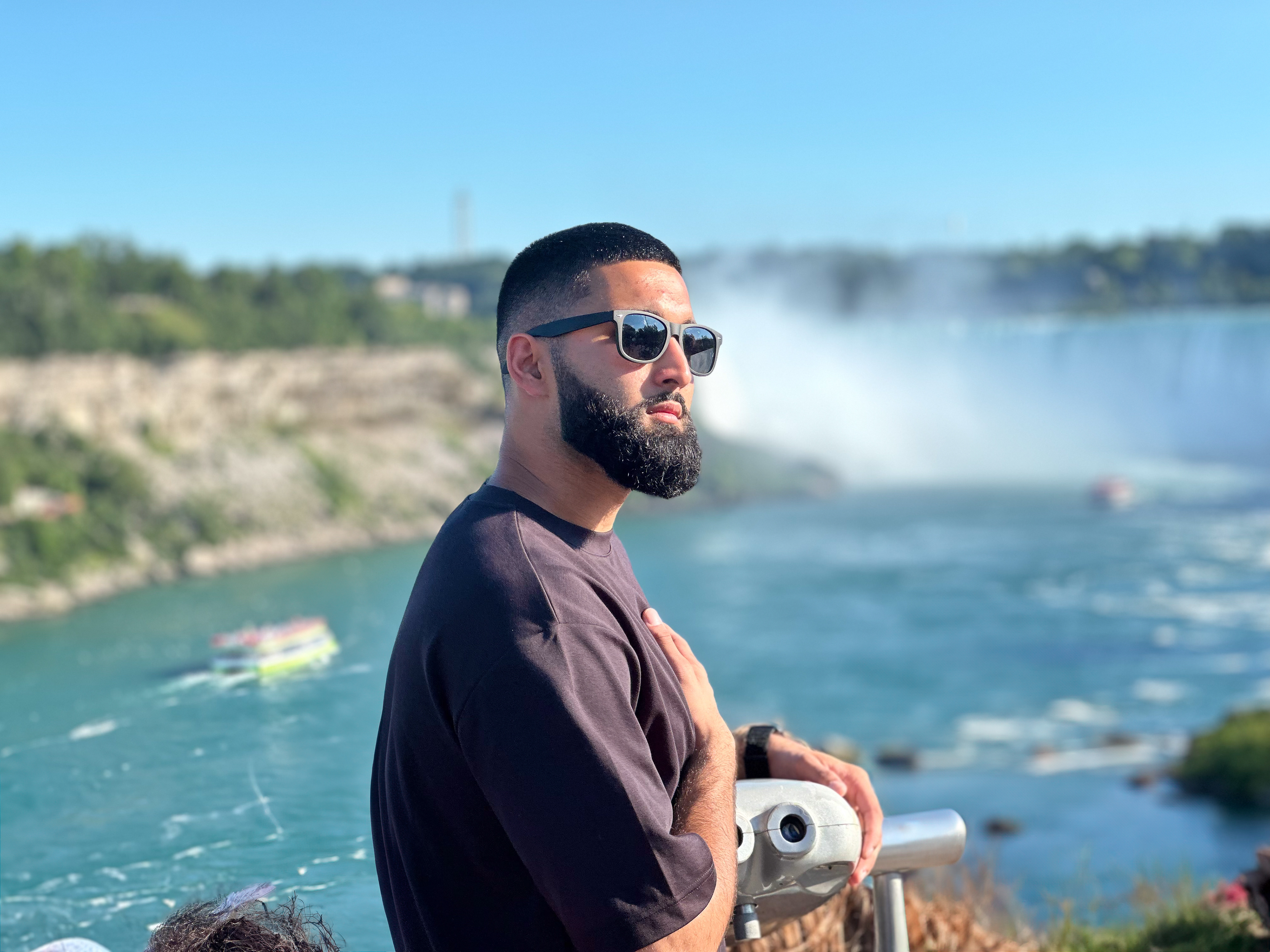 Muhammad Abbasi | Lifestyle | Black t-shirt, light blue jeans, black sneakers, side profile by railing overlooking Niagara Falls