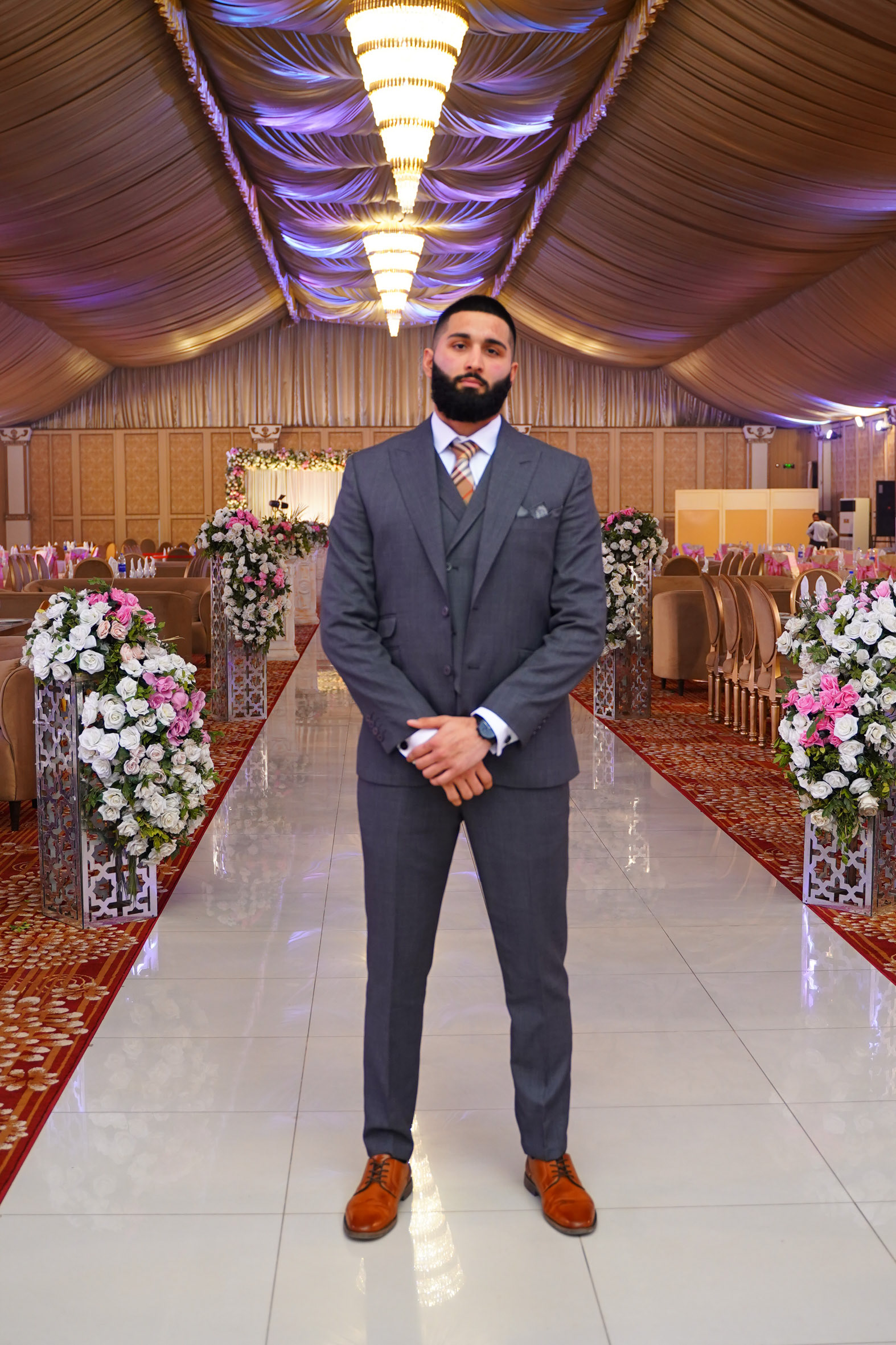 Muhammad Abbasi | Formal Wear | Charcoal three-piece suit with striped tie, standing with hands clasped