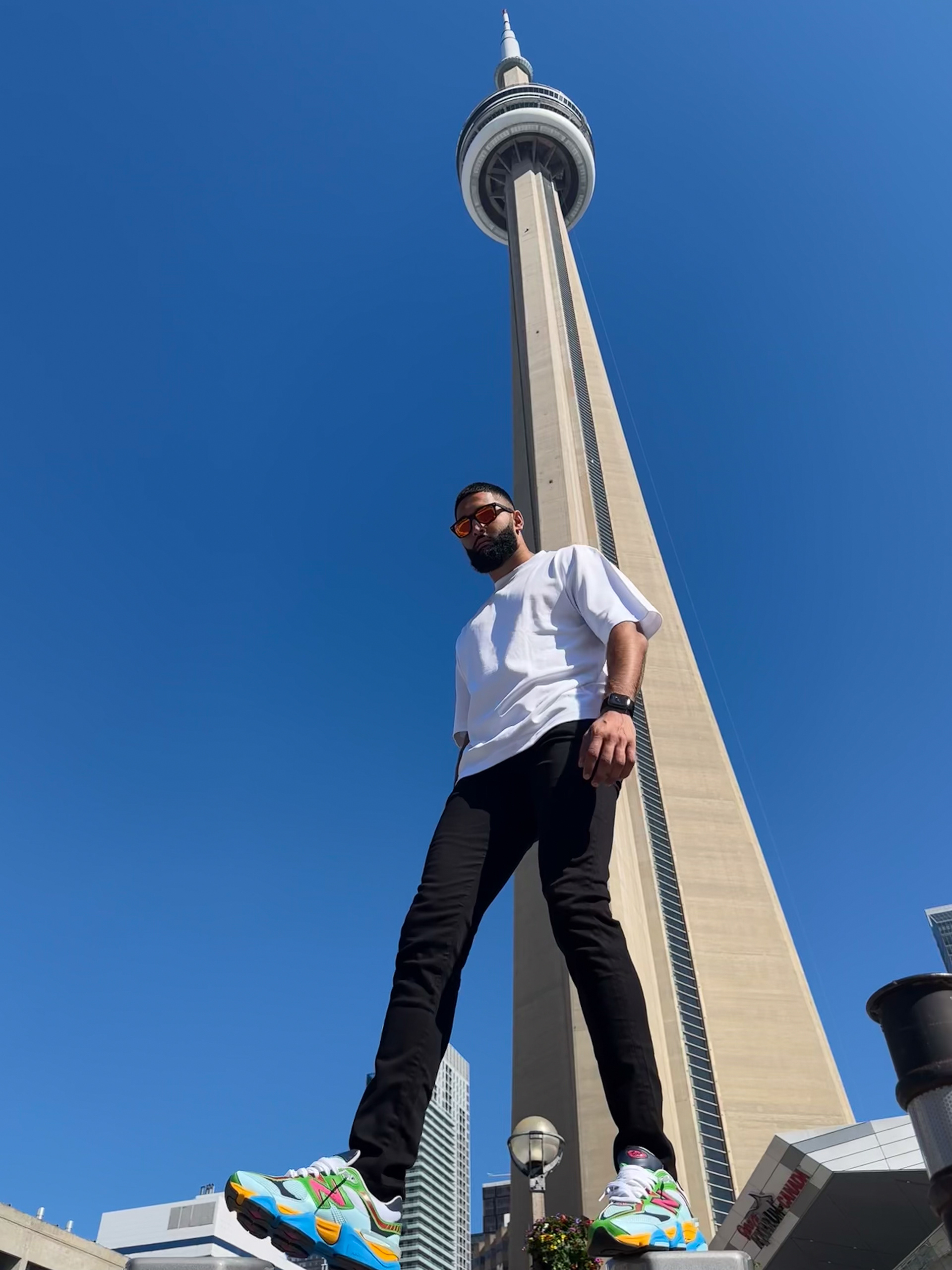 Muhammad Abbasi | Lifestyle | White oversized t-shirt, black jeans, colorful sneakers, standing with CN Tower in background