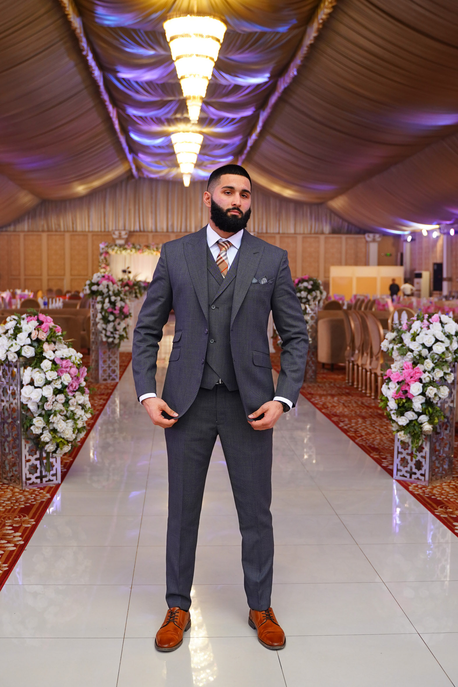 Muhammad Abbasi | Formal Wear | Charcoal three-piece suit with striped tie, standing with hands pulling blazer