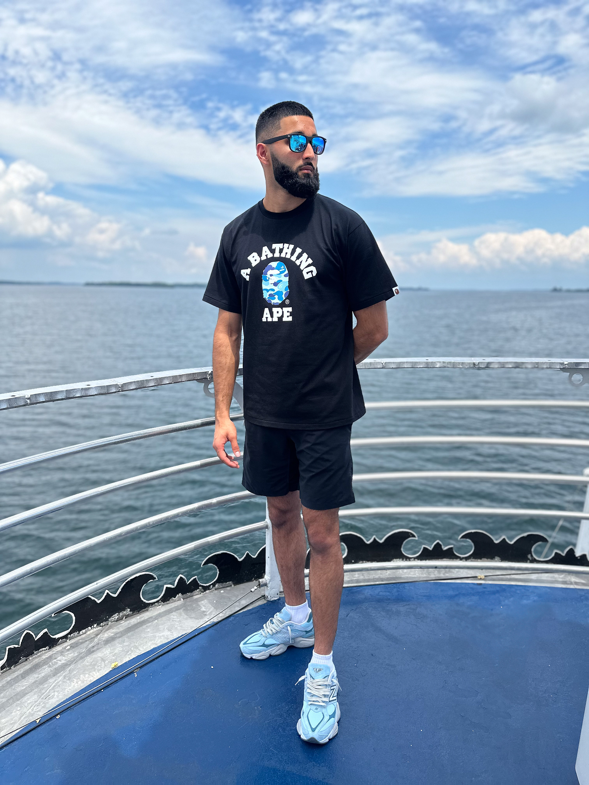 Muhammad Abbasi | Lifestyle | Black graphic t-shirt, black shorts, light blue sneakers,  on boat deck with open water view