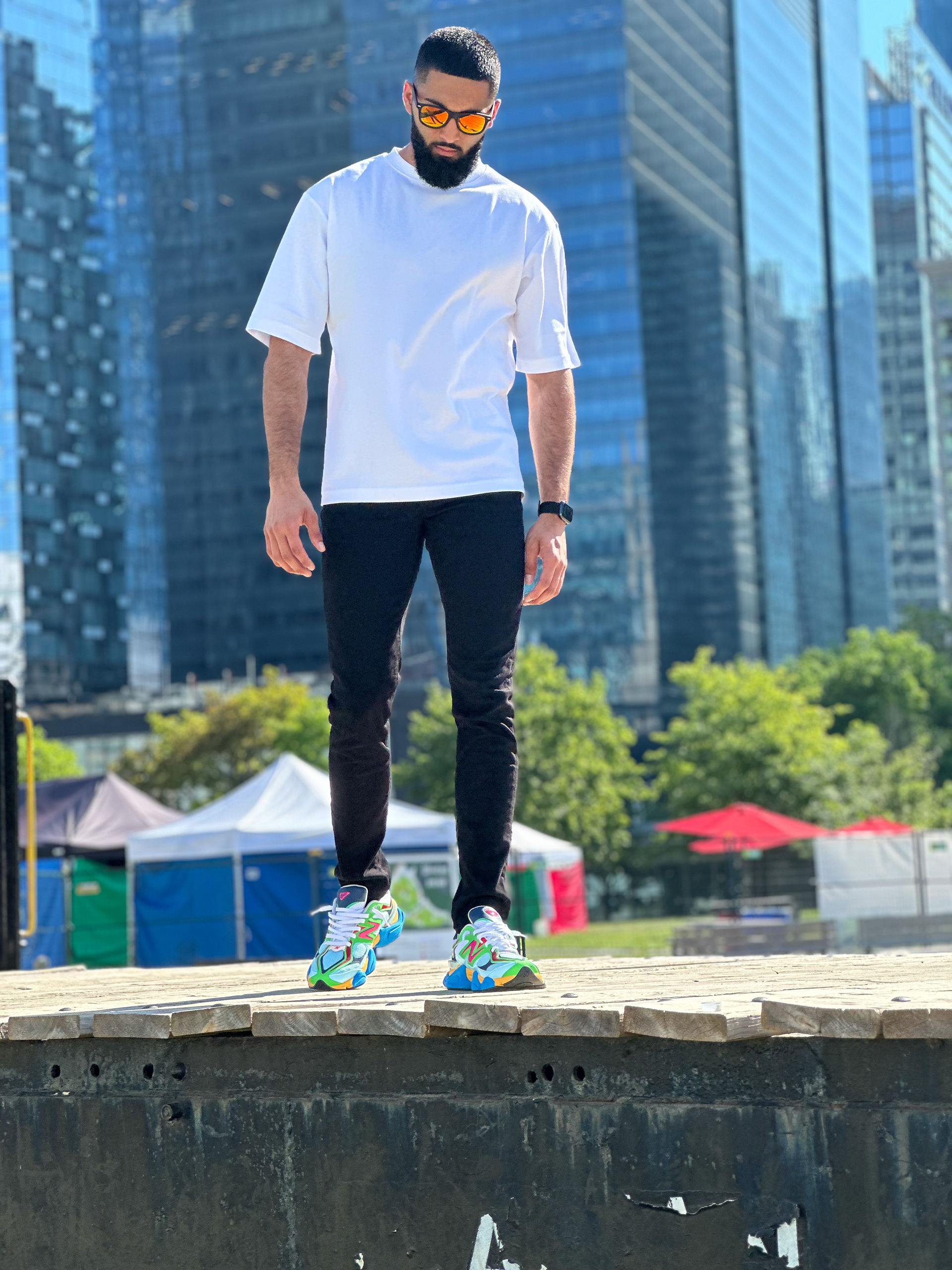 Muhammad Abbasi | Lifestyle | White oversized t-shirt, black jeans, colorful sneakers, looking down while walking on wooden dock in Toronto