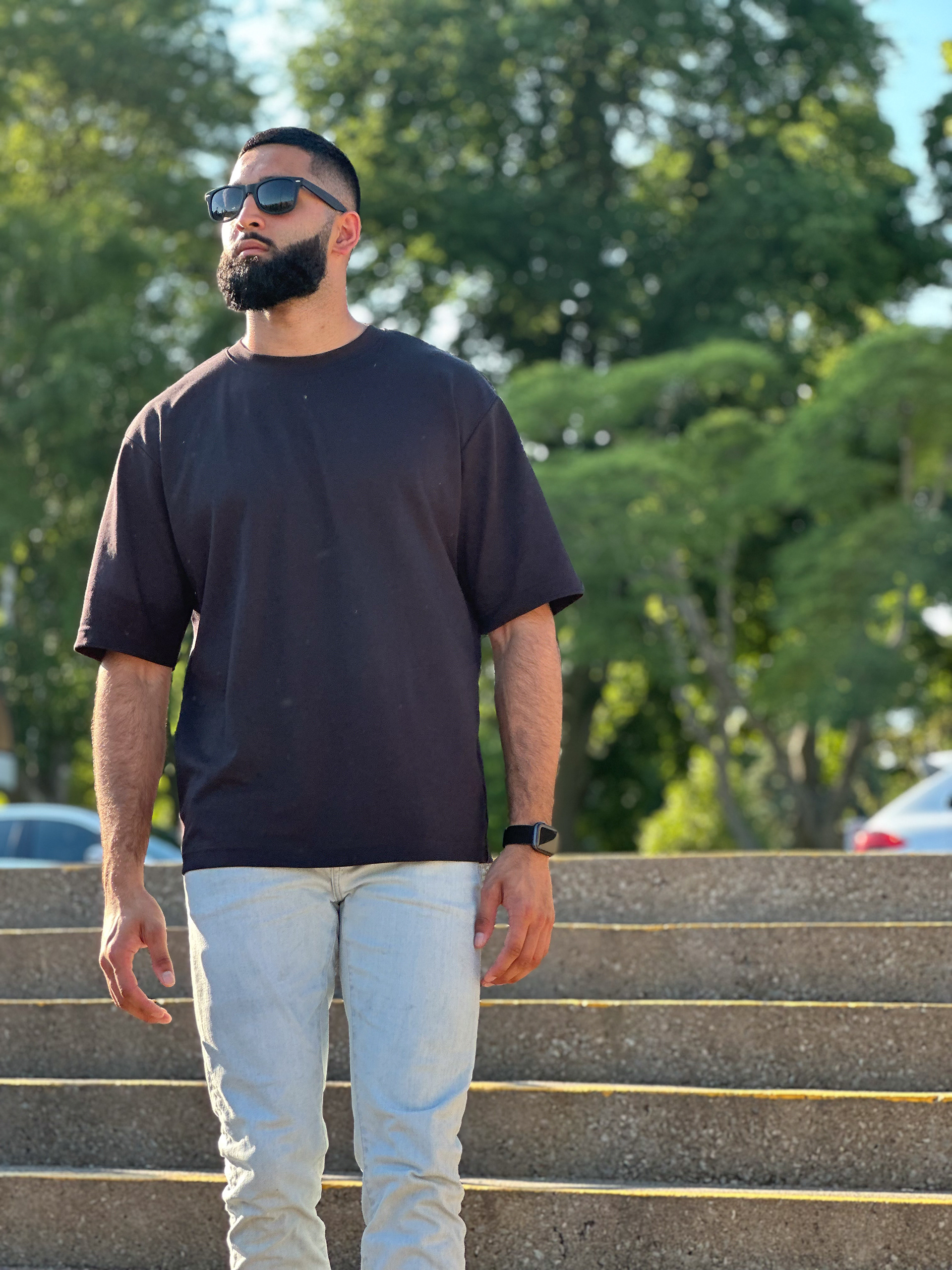 Muhammad Abbasi | Lifestyle | Black t-shirt, light blue jeans, black sneakers, front view in sunlight with trees in background